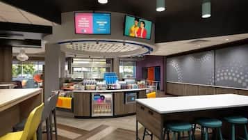 A modern cafe with a central counter, seating area, and two digital screens displaying advertisements.