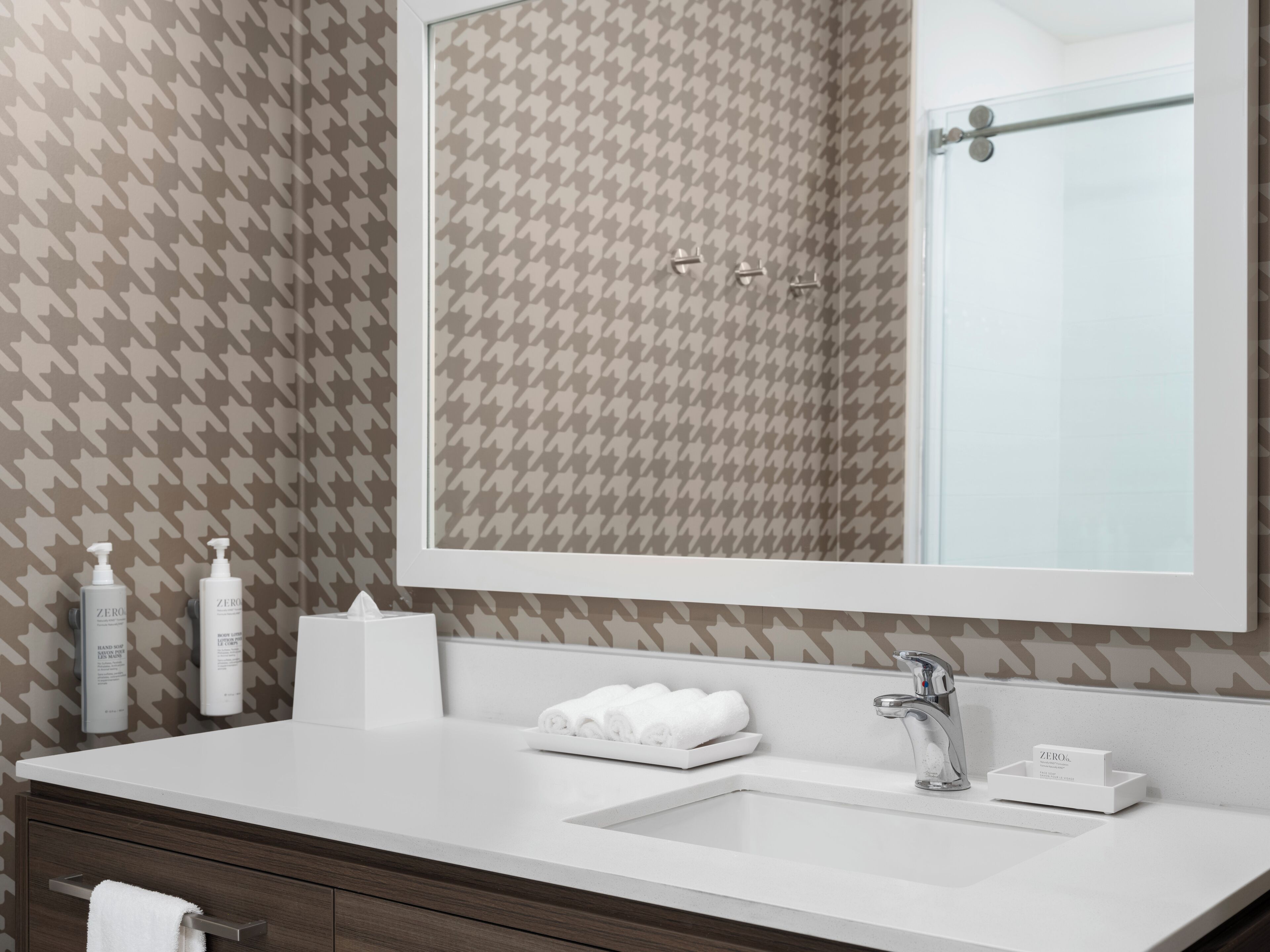 A bathroom with a houndstooth patterned wall, a white sink, a mirror, and a towel rack.
