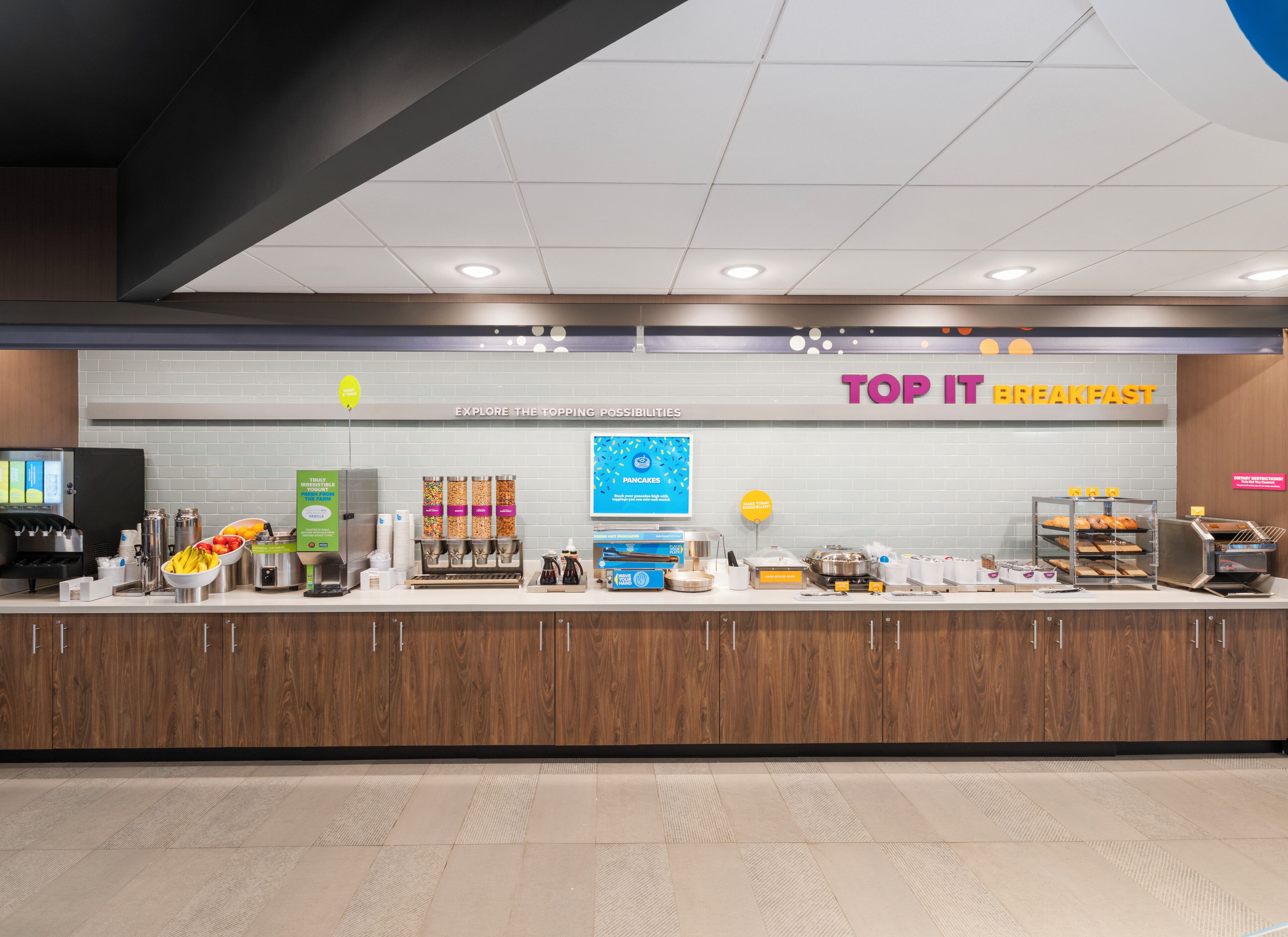 A breakfast area with a counter displaying various food items and a sign that reads 'TOP IT BREAKFAST'.