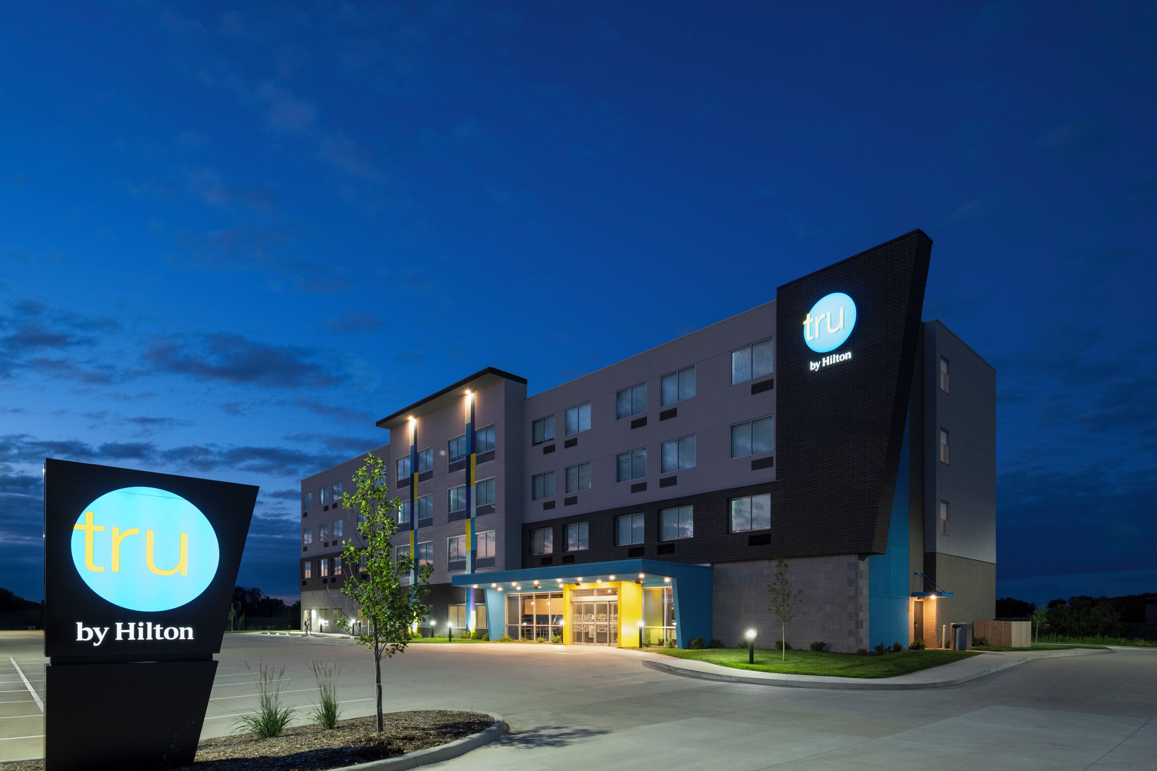 Un moderno edificio de hotel con un llamativo letrero de 'tru by Hilton', varios pisos y una entrada bien iluminada.