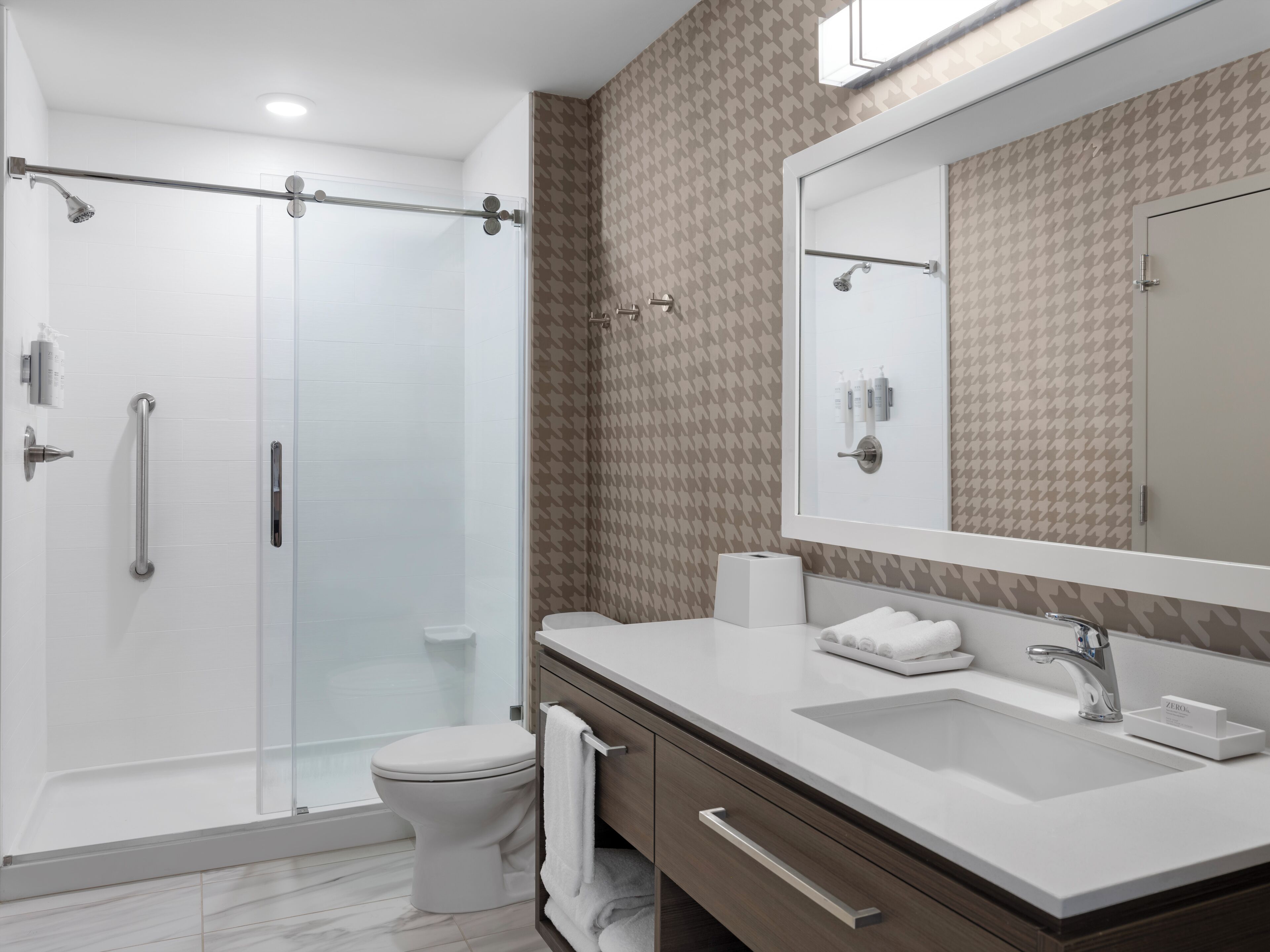Een moderne badkamer met een douchecabine van glas, een wit toilet, een wastafelmeubel met een grote spiegel en een wastafel.