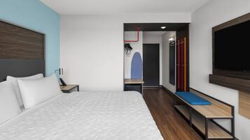 A modern hotel room with a large bed, a desk, a bench, and a TV mounted on the wall.