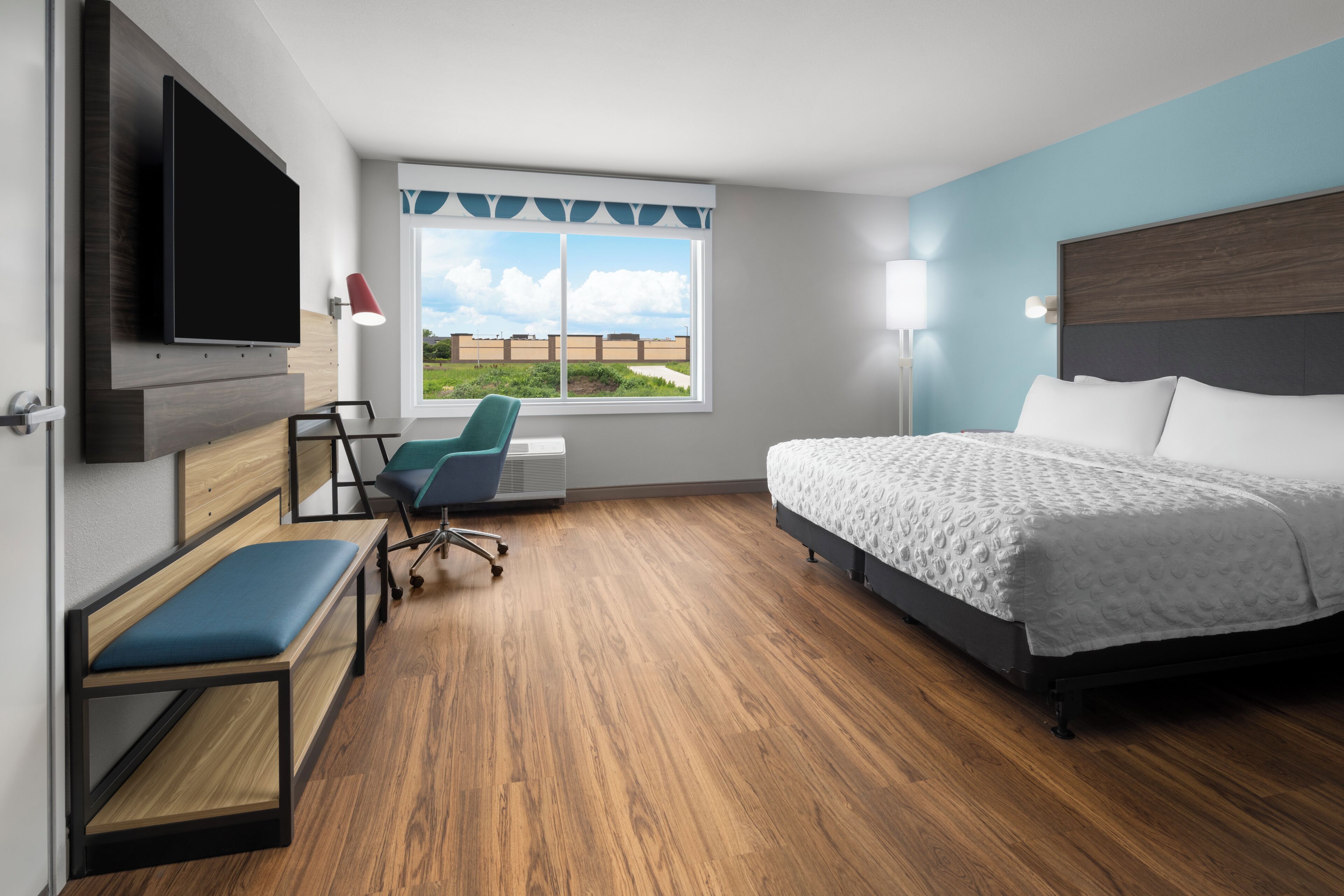 Habitación de hotel con cama, escritorio, silla, televisor y ventana con vistas.