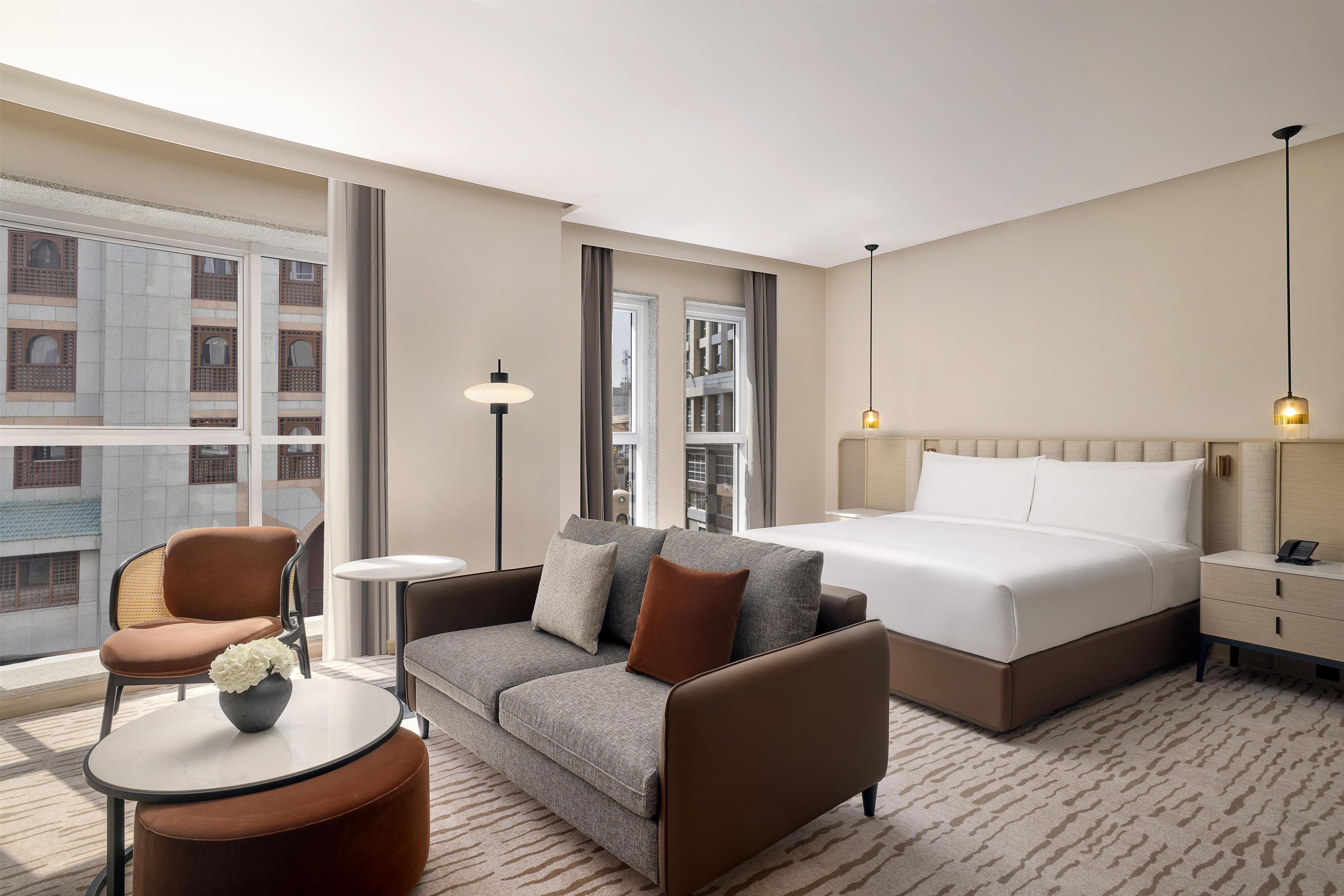 A hotel room with a bed, a sofa, a chair, a small table, and a lamp.