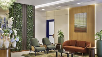 A modern living room with a sofa, two armchairs, a coffee table, and a decorative wall with greenery and a painting.