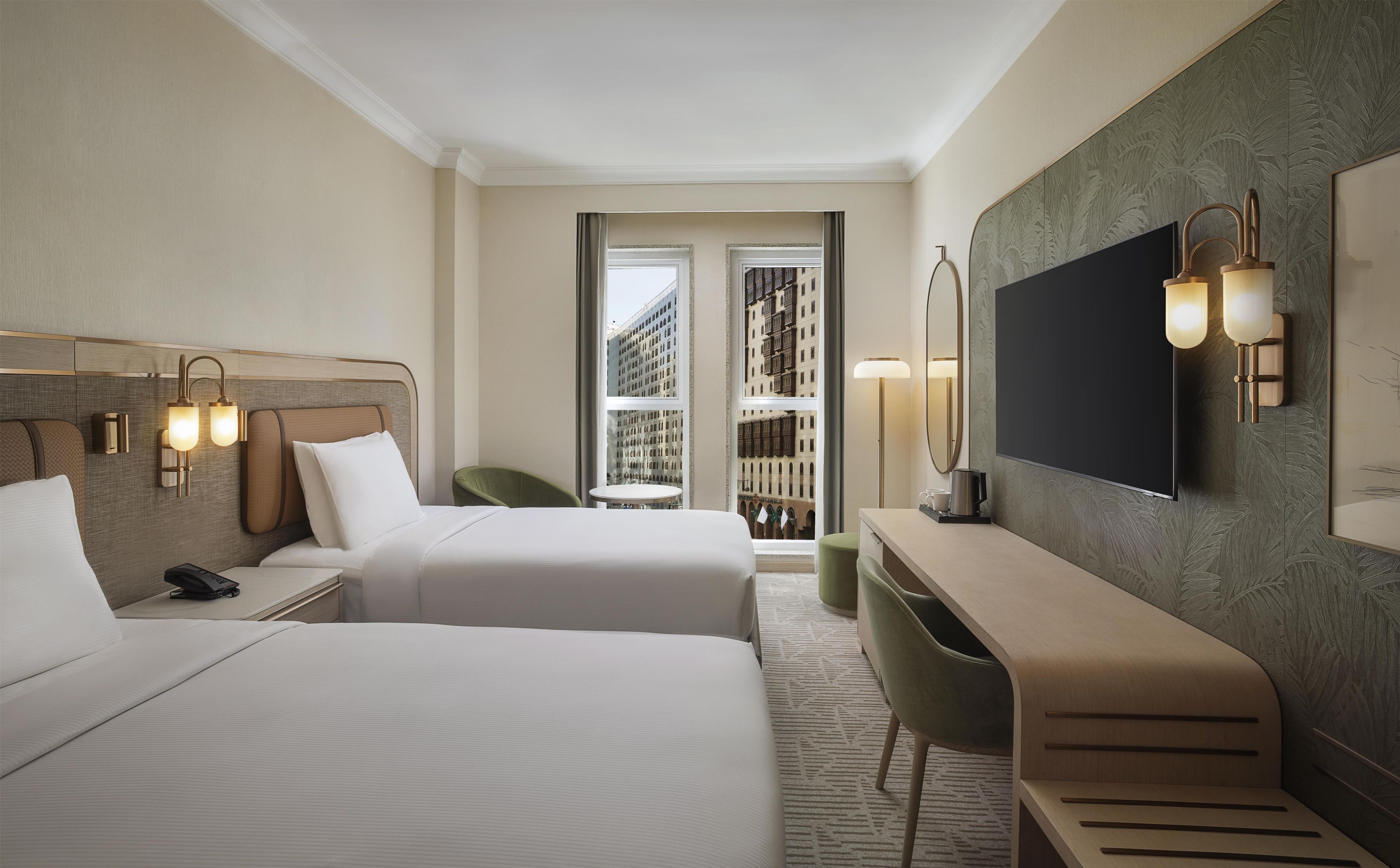 Une chambre d’hôtel avec deux lits, un bureau, une chaise, une télévision et une vue sur les bâtiments par la fenêtre.