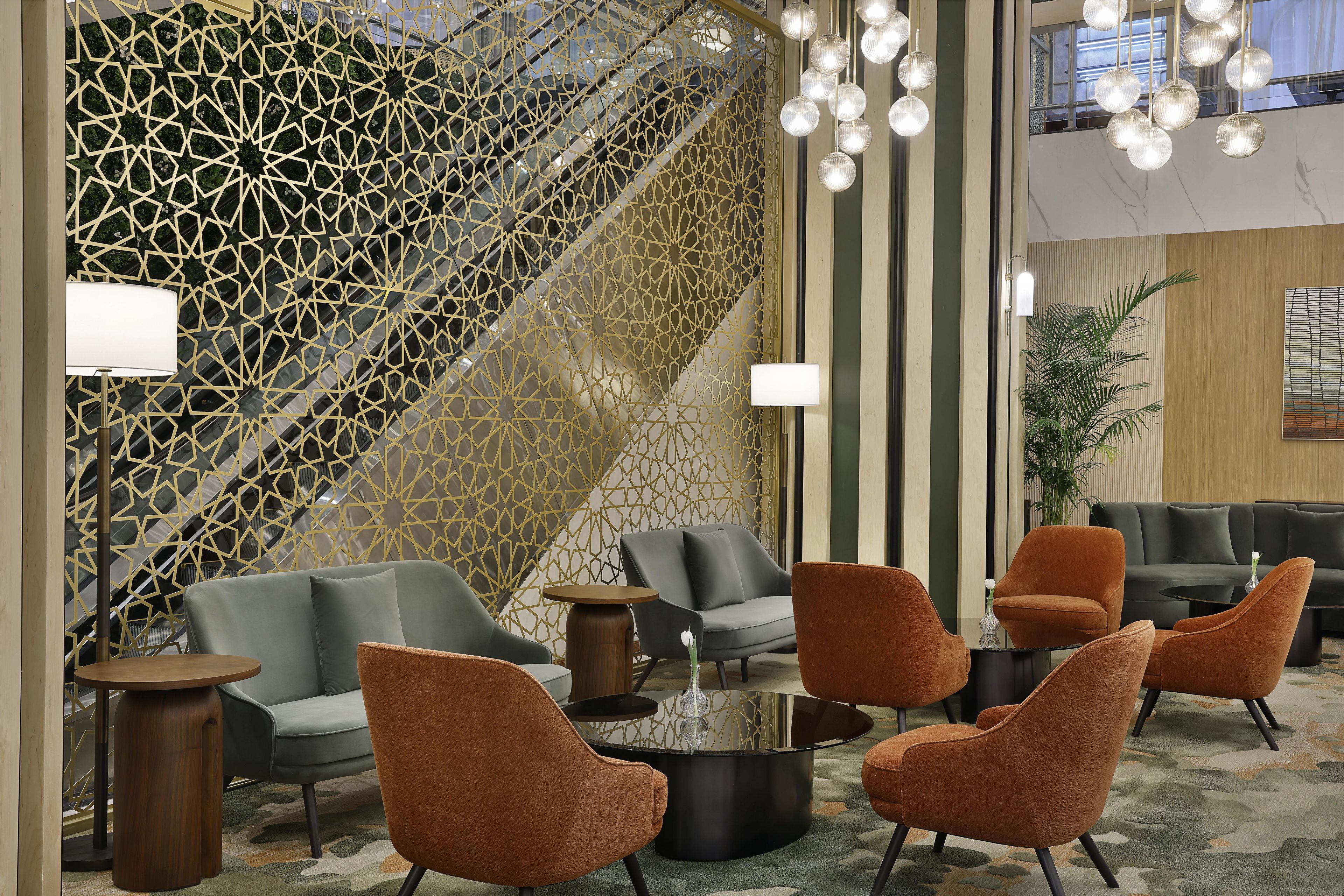 Un vestíbulo moderno con un muro de diseño geométrico, zona de estar con sofás y sillones, una mesa de centro y una escalera con barandilla decorativa.