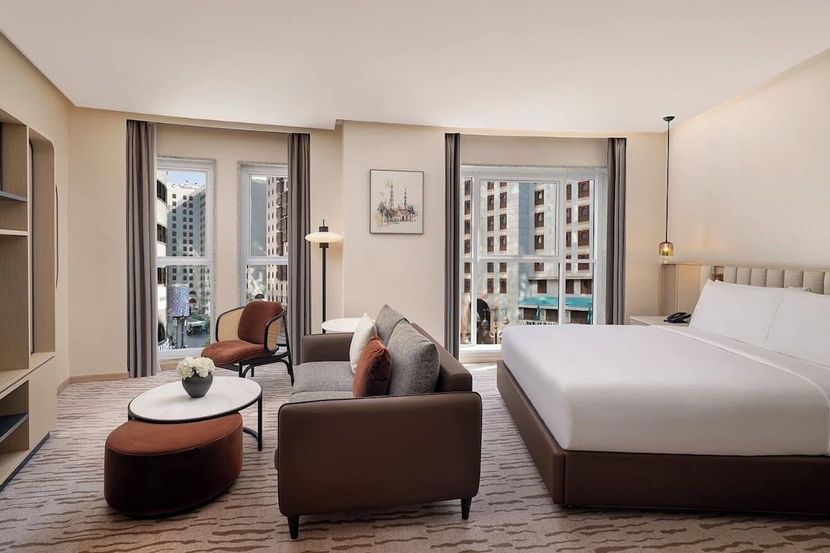 Una habitación de hotel con cama, sofá, sillón, una mesita y televisor.