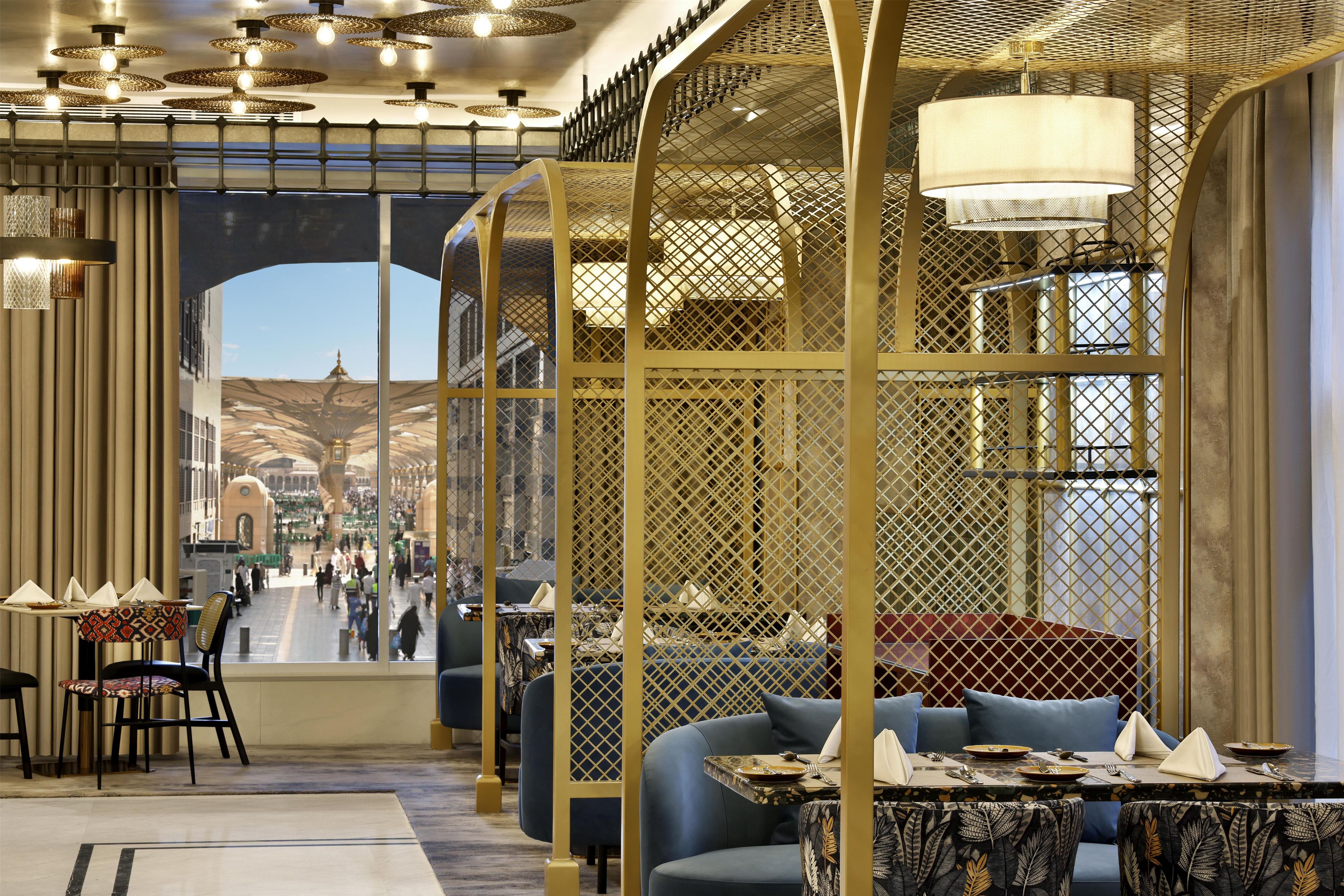 A modern restaurant interior with high ceilings, decorative lighting, and a view of a busy street through an open archway.