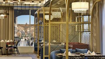 A modern restaurant interior with high ceilings, decorative lighting, and a view of a busy street through an open archway.