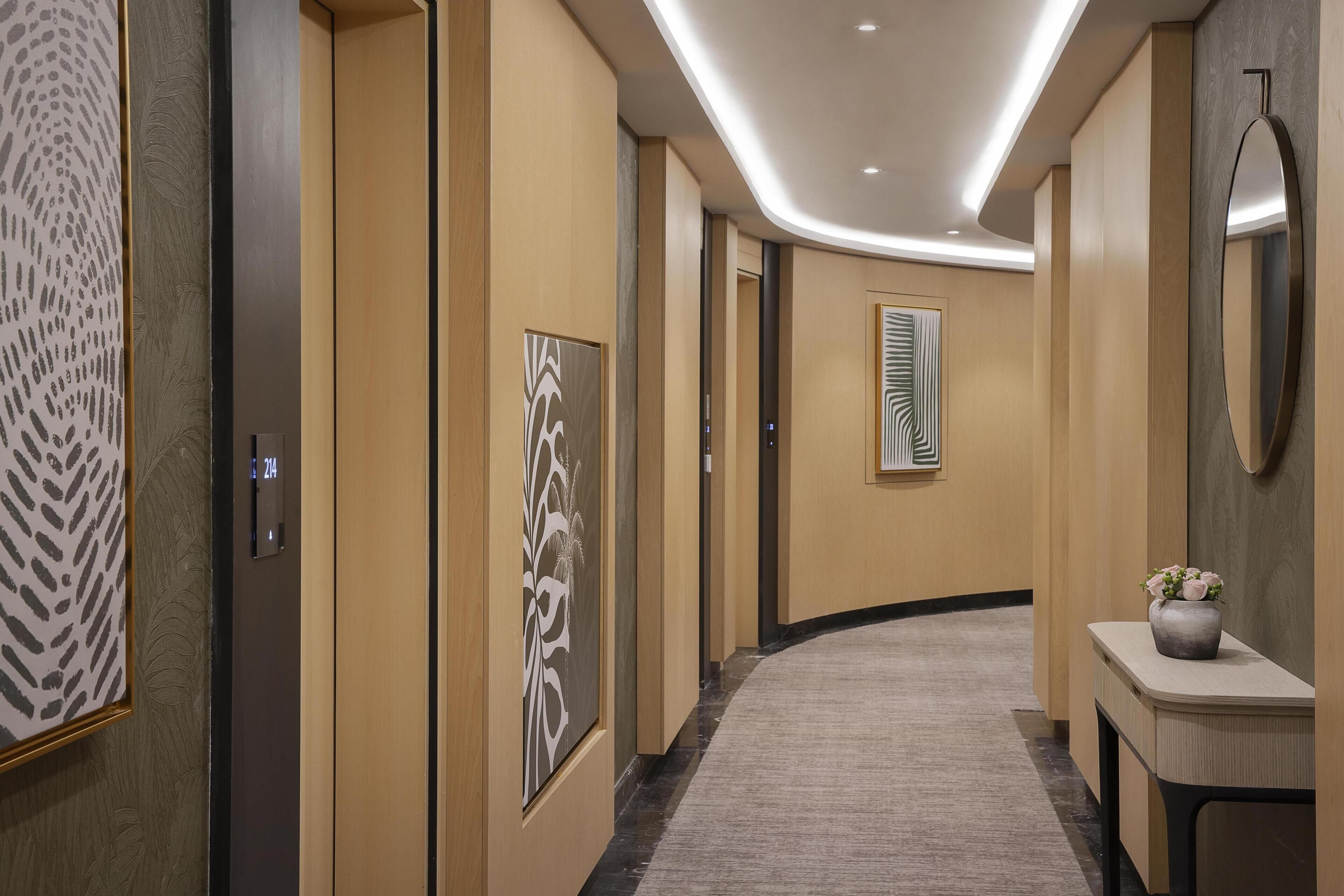 Un pasillo moderno de hotel con alfombra curva, paneles de madera y cuadros en las paredes.