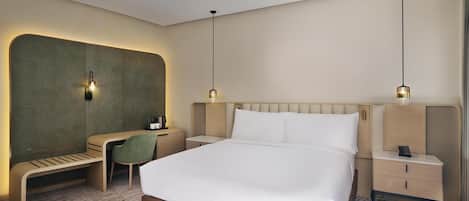 Ein modernes Hotelzimmer mit einem großen Bett, einem Schreibtisch, einer Bank und zwei Nachttischen mit Lampen.
