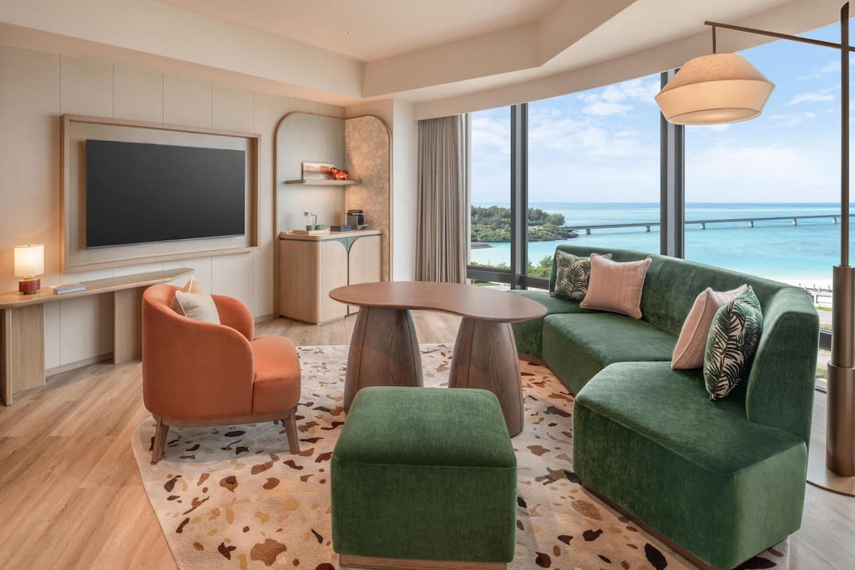 A modern living room with a large TV, a sofa, a coffee table, and a view of the ocean.
