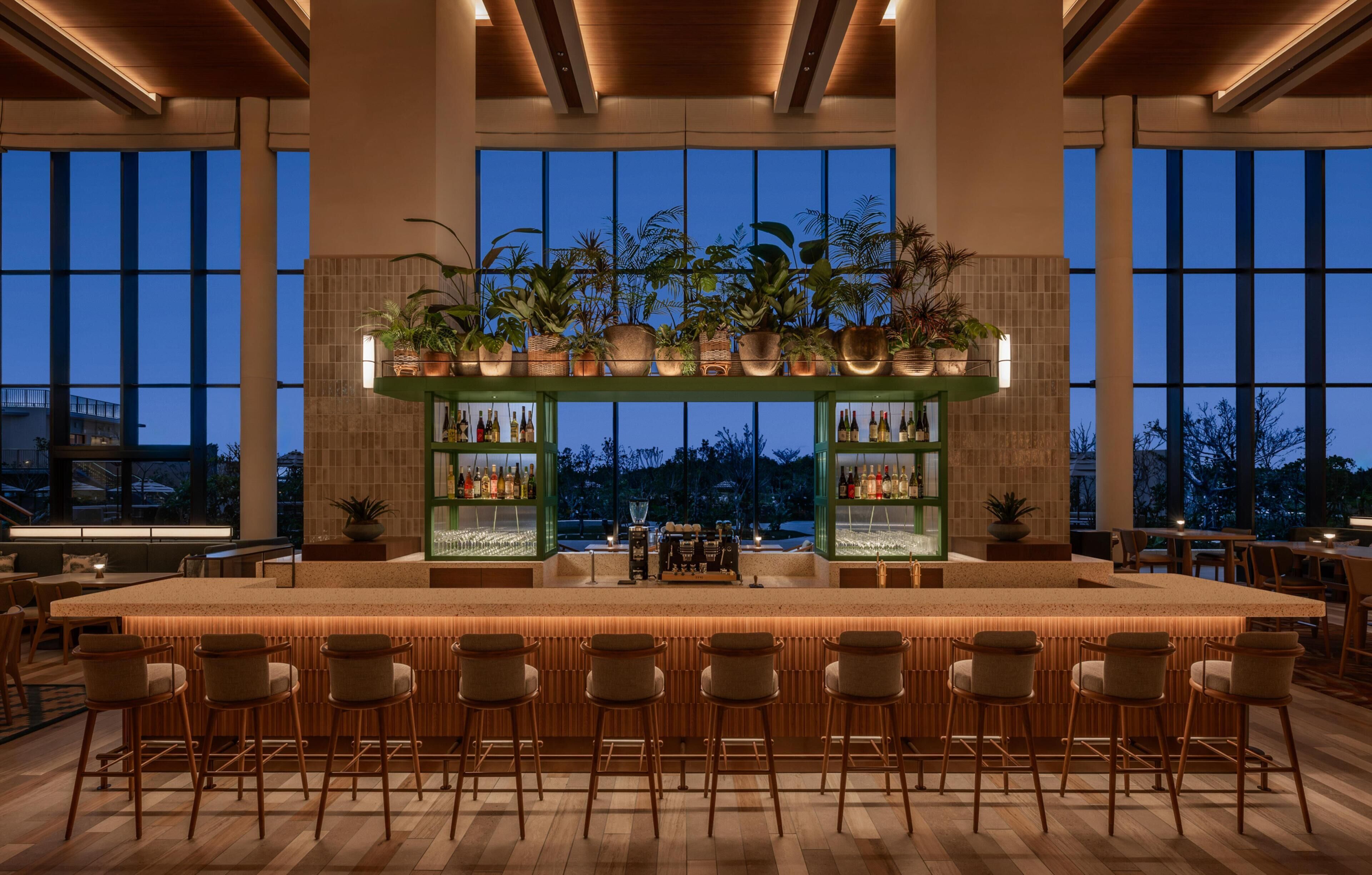 A bar area with a long counter, multiple stools, and shelves with bottles.