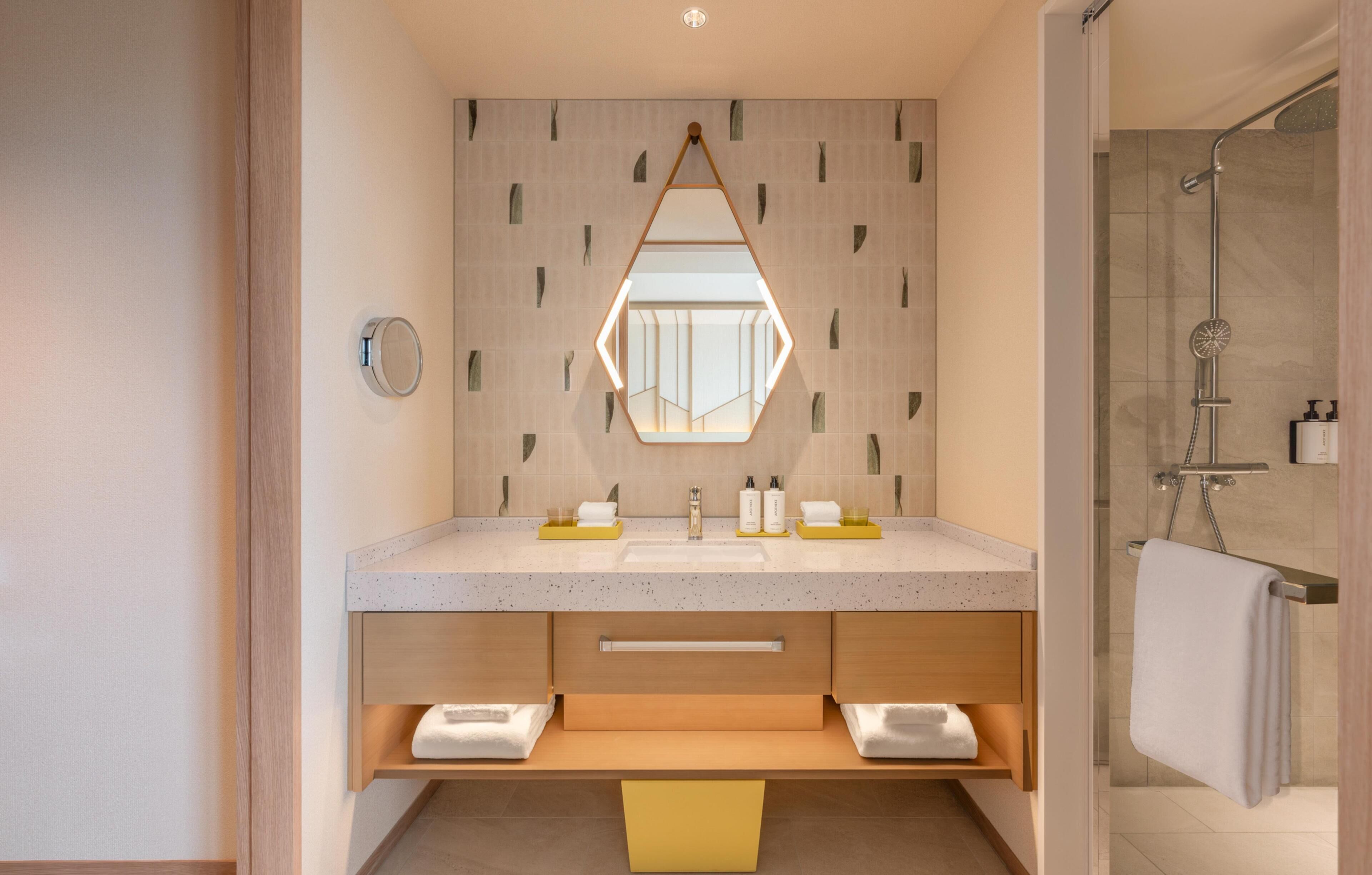 Un baño moderno con un espejo hexagonal, dos lavamanos, una ducha y un perchero para toallas.