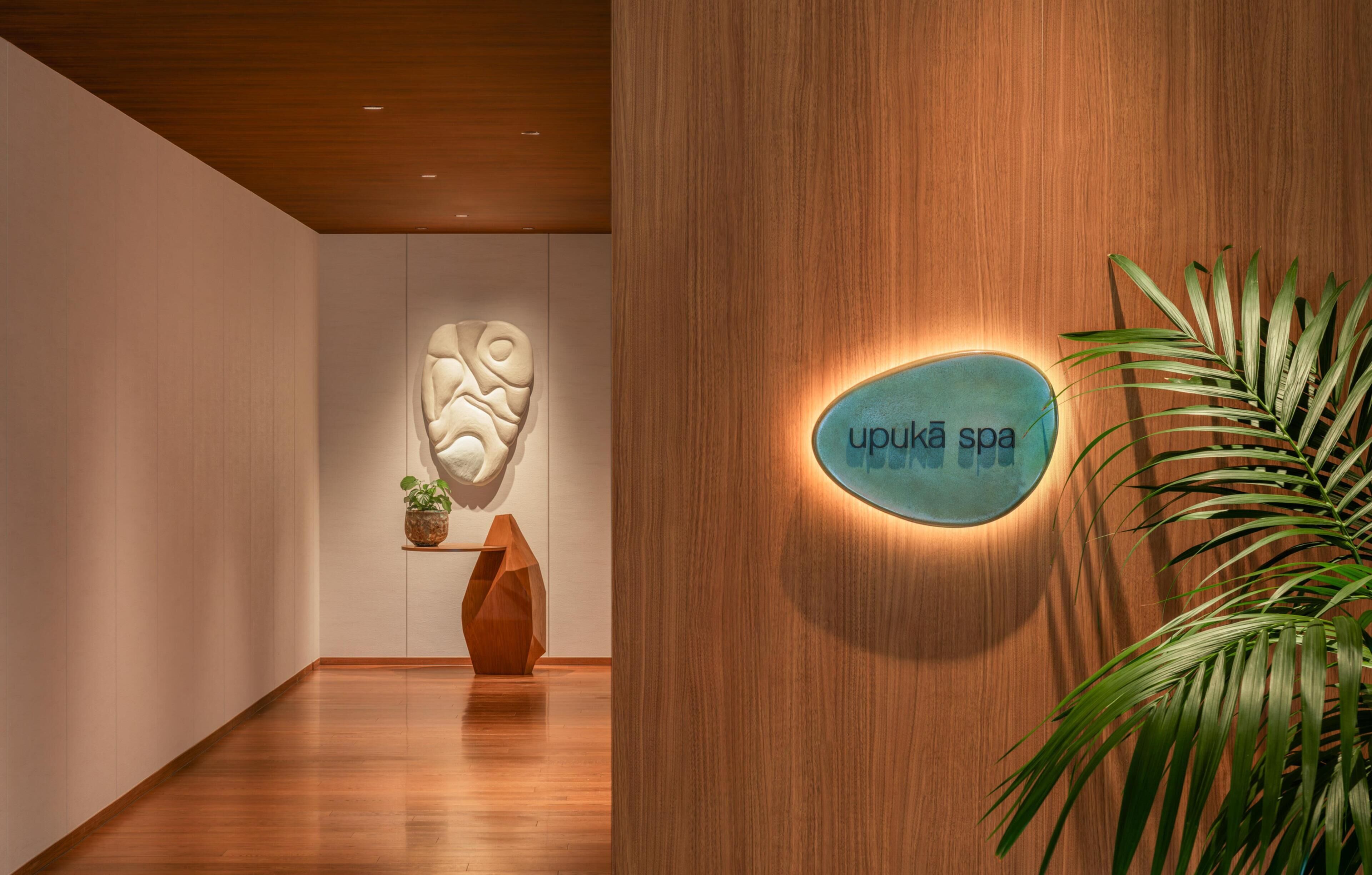 A spa interior with a wooden wall, a sign reading 'upukā spa,' and a potted plant.
