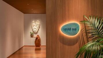 A spa interior with a wooden wall, a sign reading 'upukā spa,' and a potted plant.