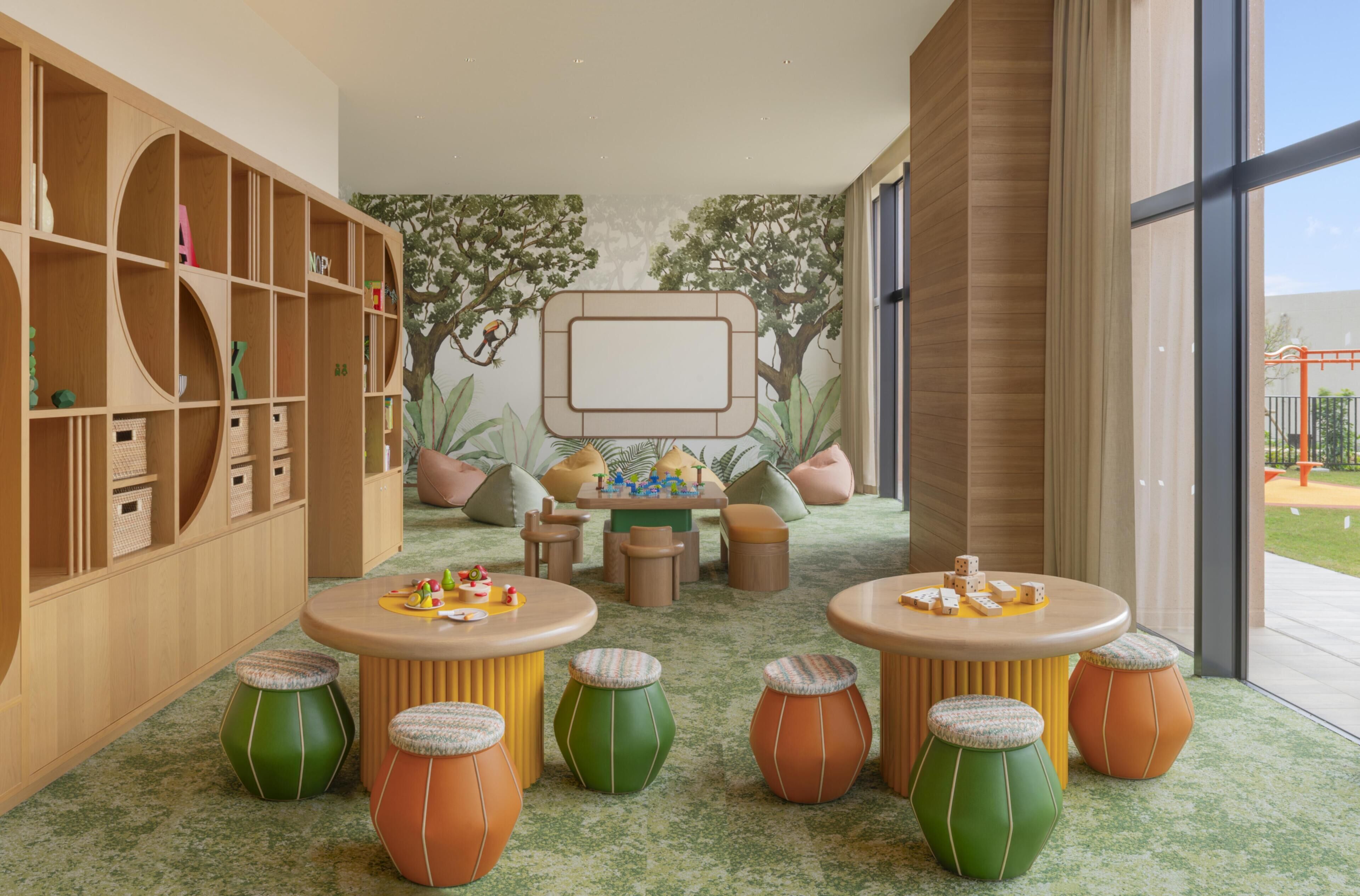 Une salle de jeux pour enfants avec une grande bibliothèque, des tabourets colorés et une fresque représentant des arbres.