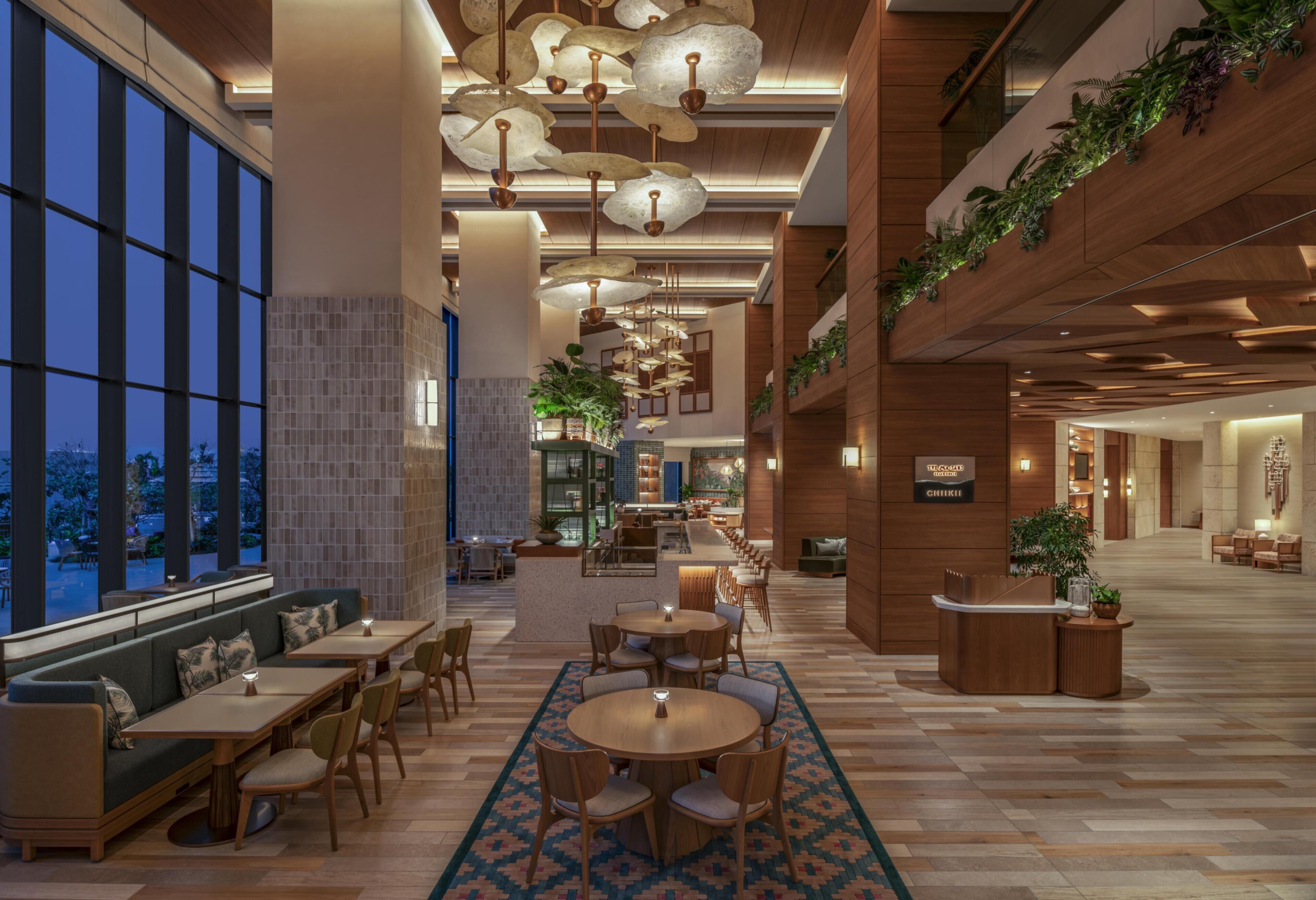 A modern hotel lobby with a central seating area, a reception desk, and a view through large windows.