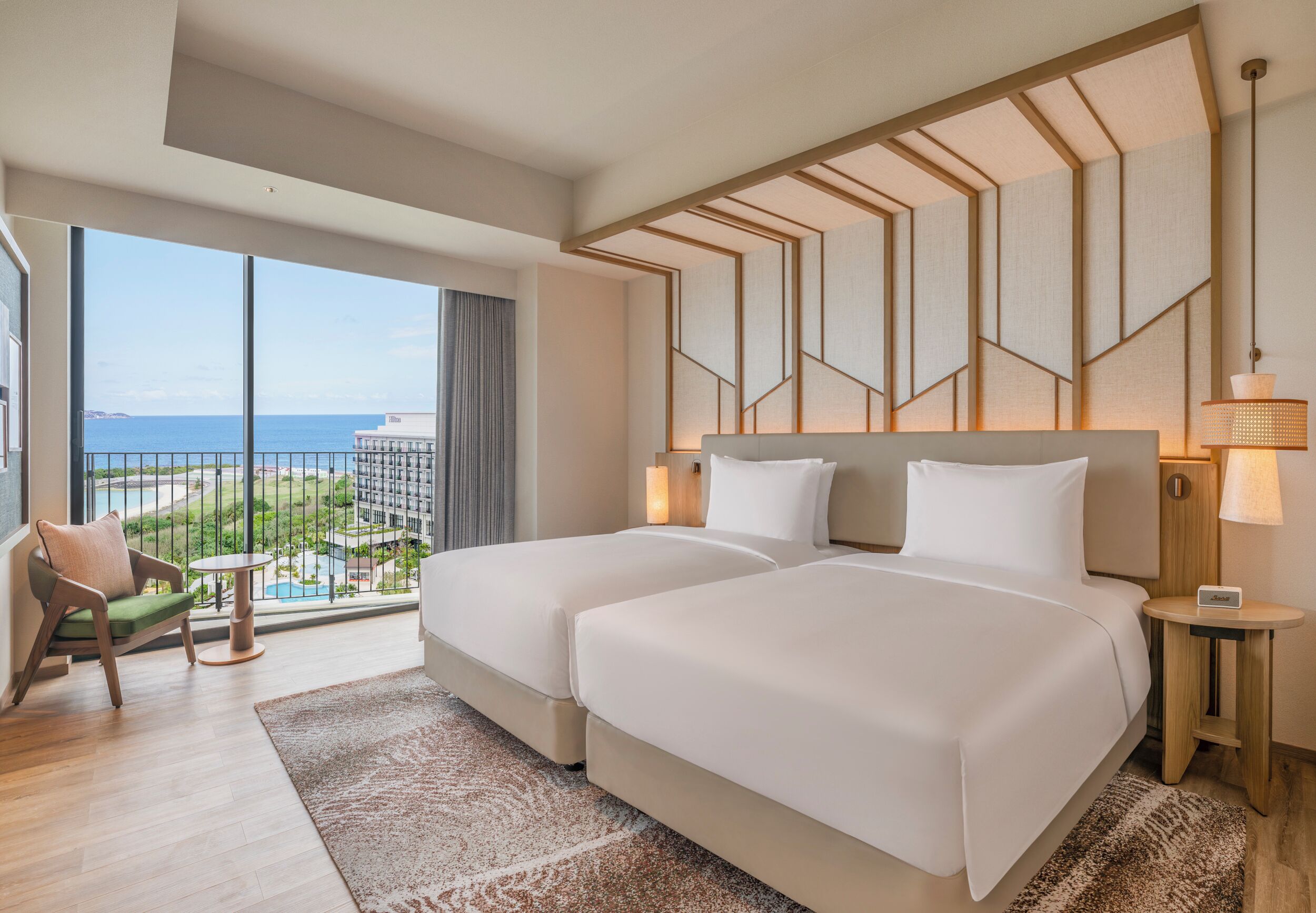 Une chambre d’hôtel avec deux lits, une vue sur l’océan, une chaise, une petite table et une lampe.