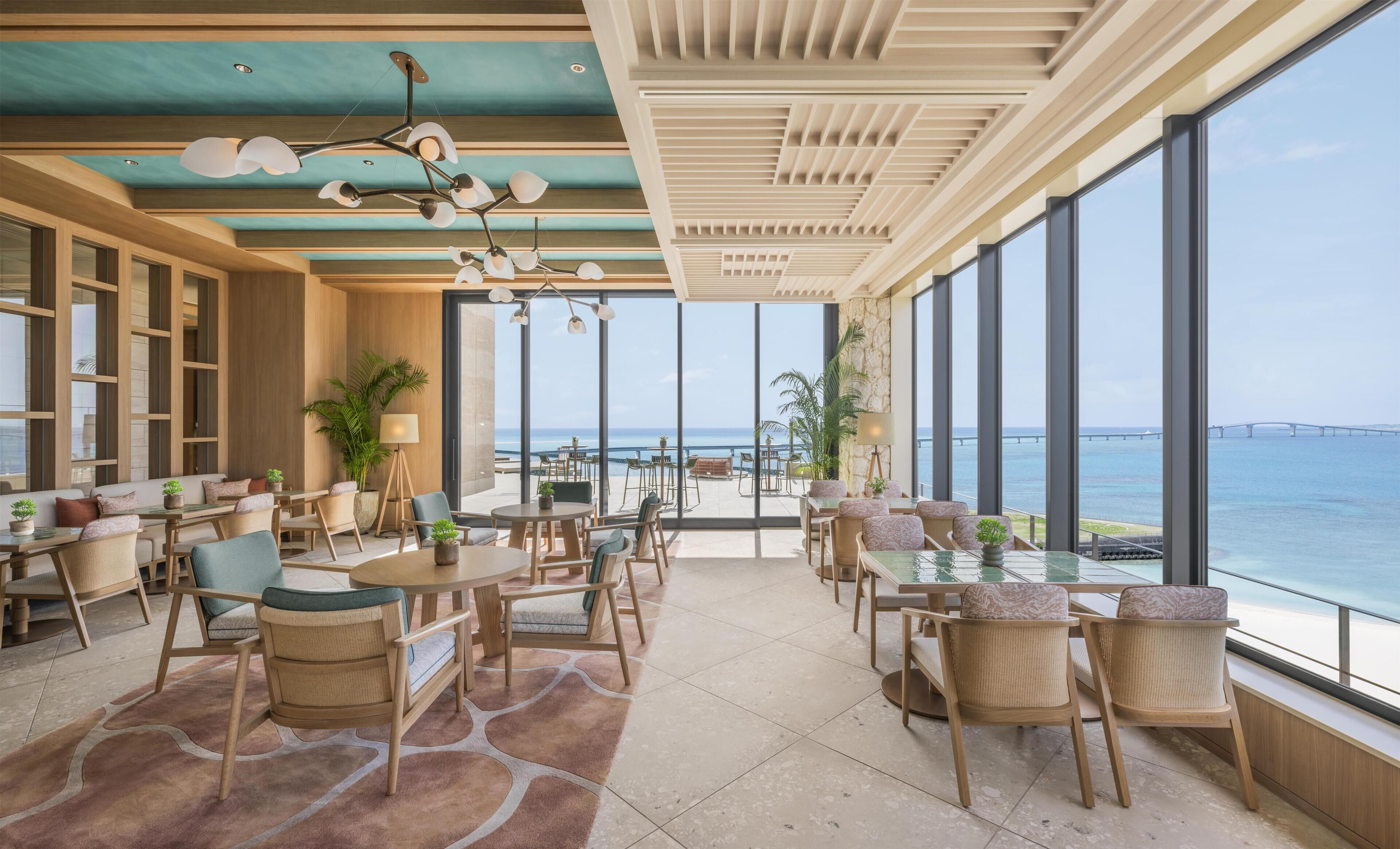 A spacious dining area with large windows overlooking the sea, featuring wooden furniture and a modern ceiling design.