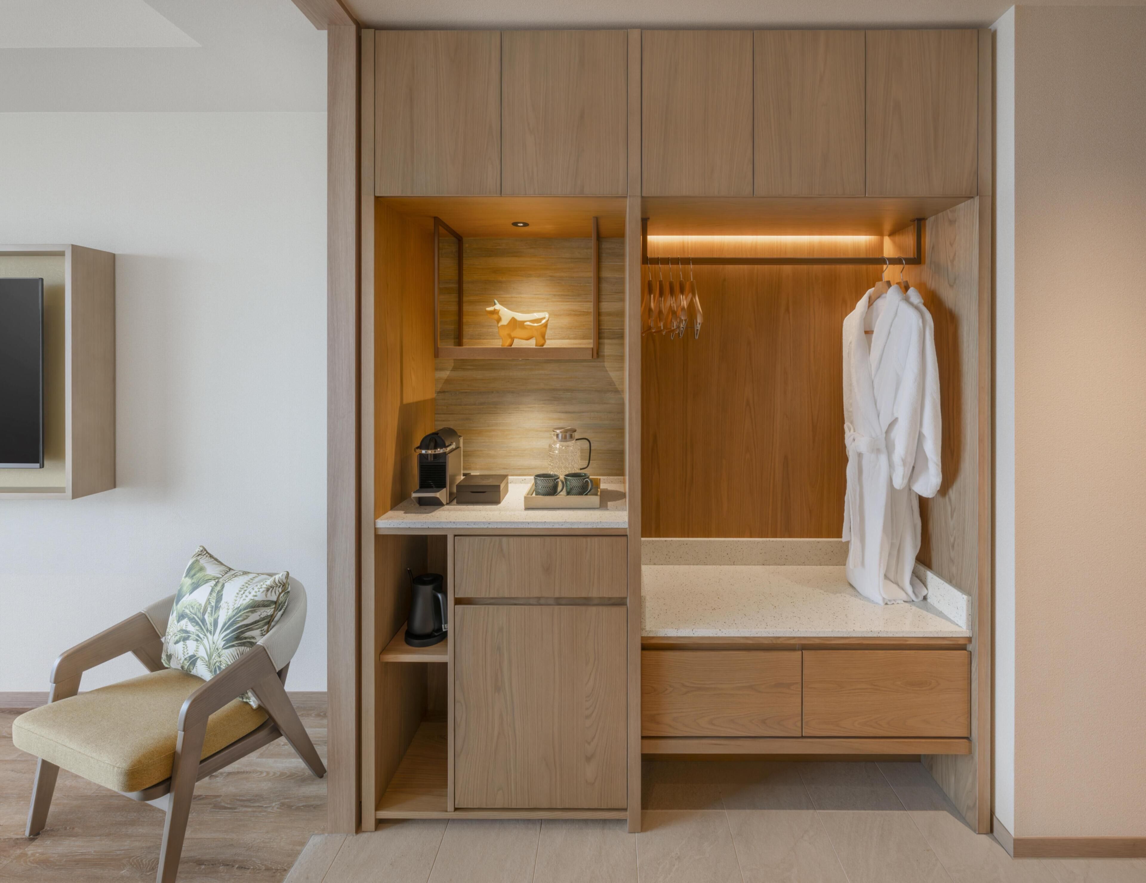 Une pièce compacte dotée d’un bureau intégré, d’un coin salon et d’un dressing avec un miroir et un espace pour suspendre les vêtements.