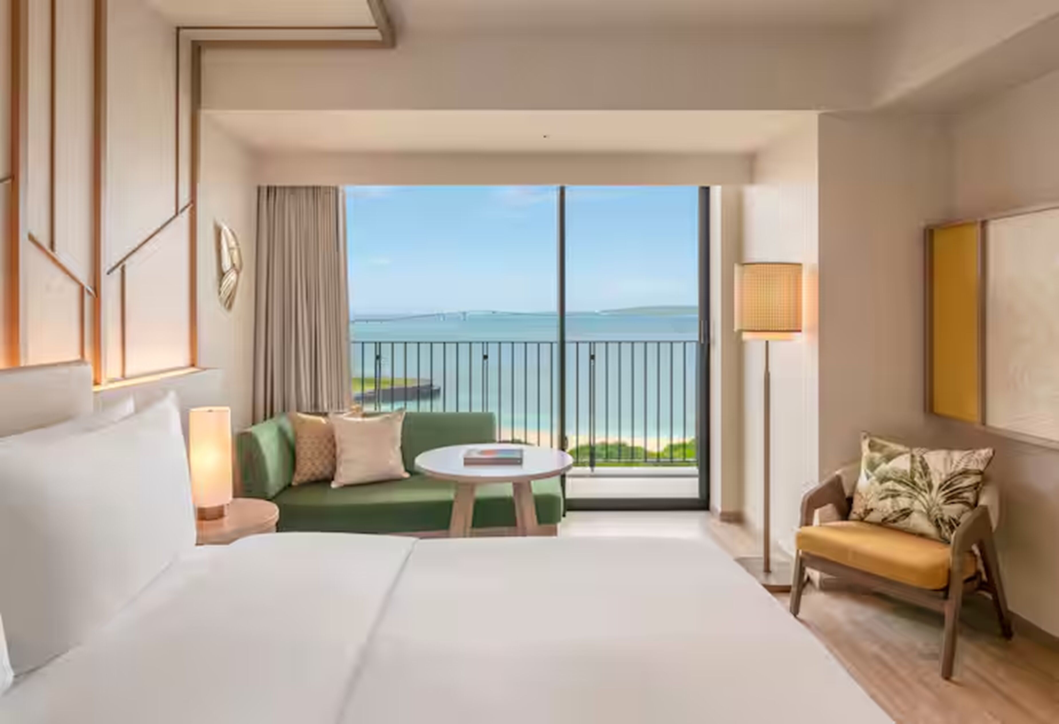 Une chambre d’hôtel avec un grand lit, un canapé vert, une petite table ronde, une chaise et un balcon avec vue sur la mer.