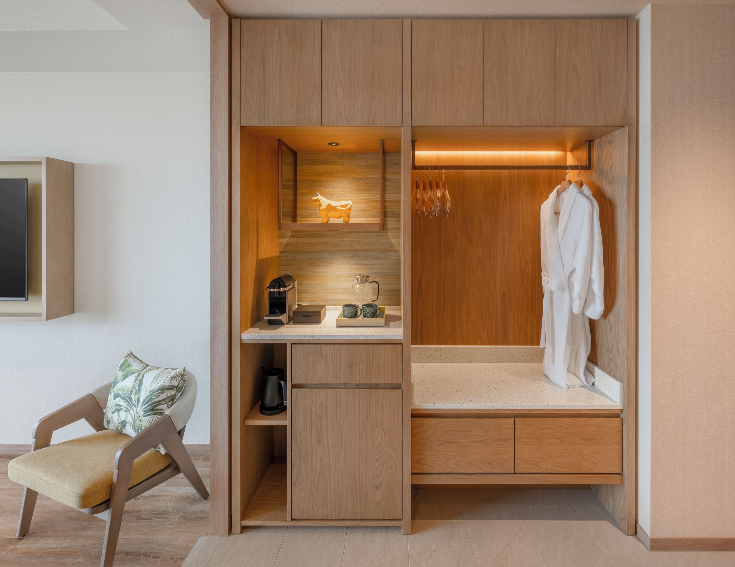 A compact bedroom with a built-in desk, a small seating area, and a walk-in closet.
