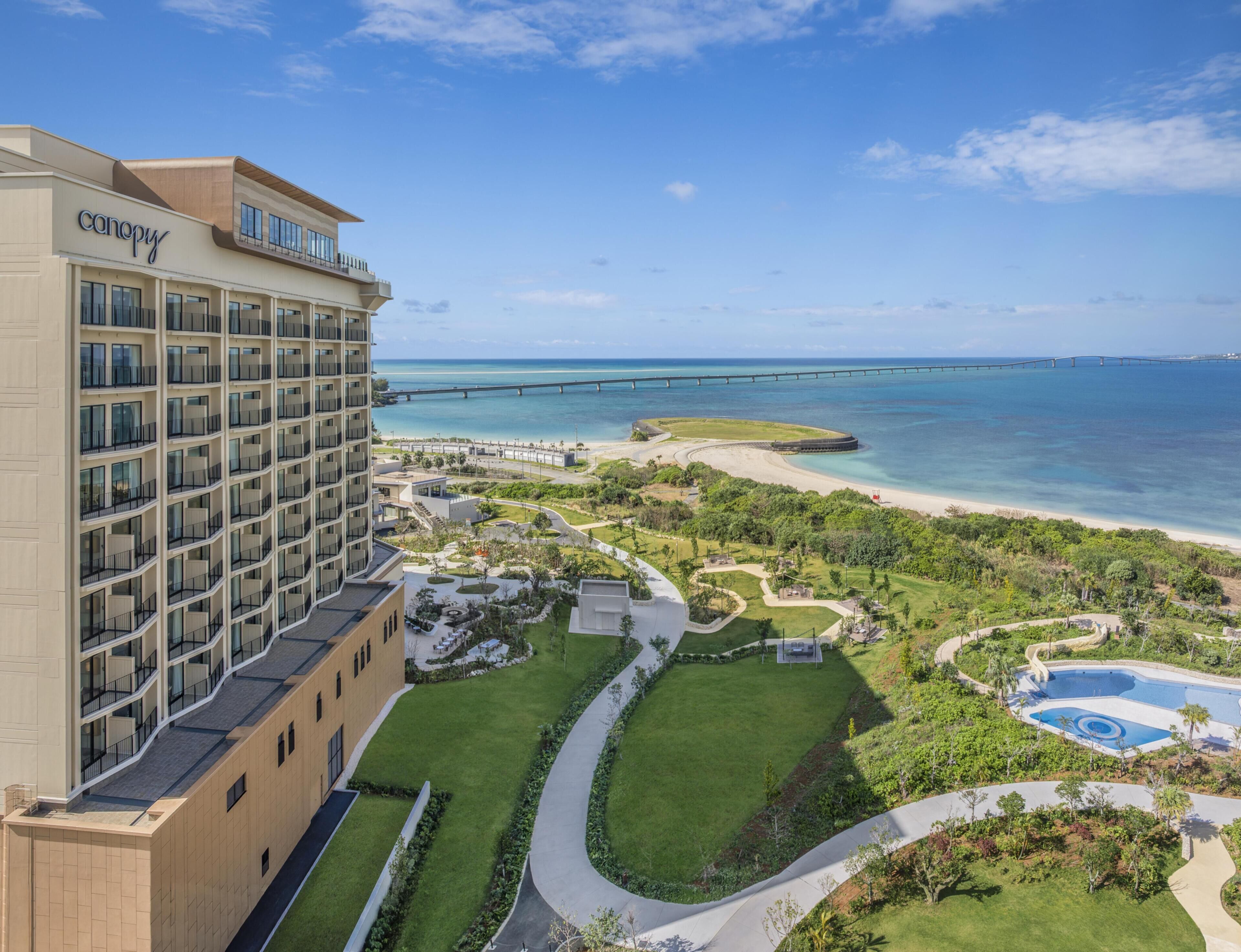 A hotel with multiple balconies, a pool area, and a view of the ocean and a bridge.