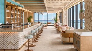 A bar area with a long counter, bar stools, and a view of the ocean. - Canopy By Hilton Okinawa Miyako Island Resort (Miyakojima)