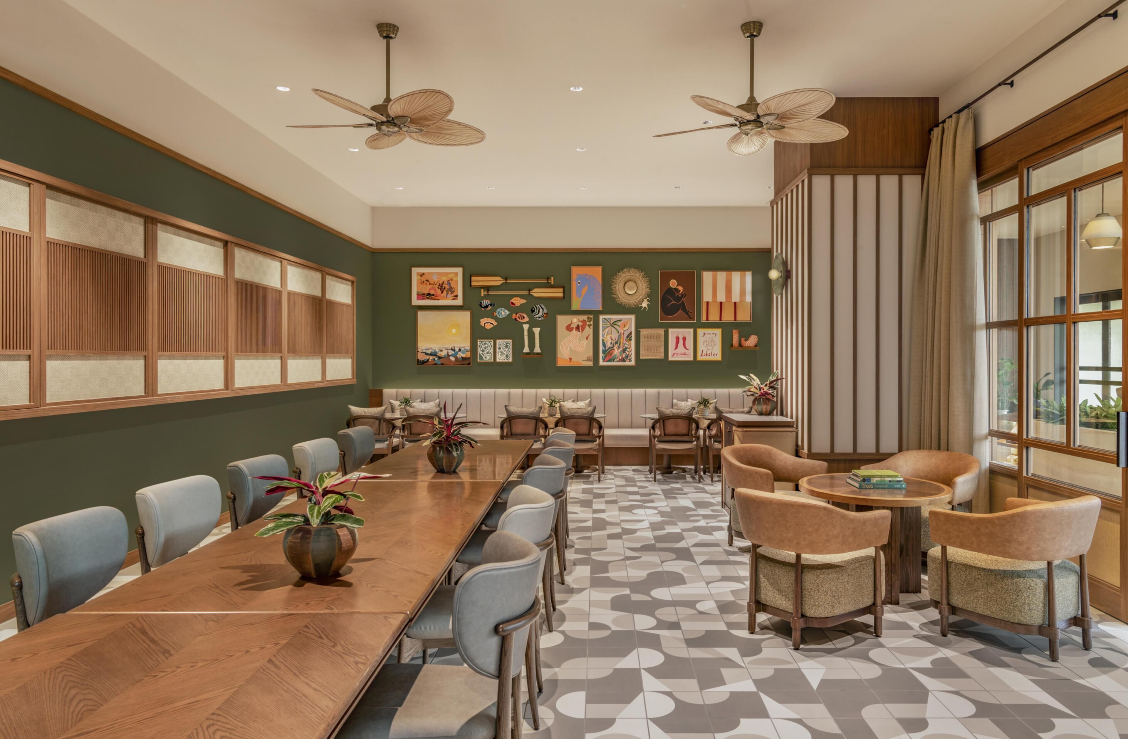 A conference room with a long table, chairs, ceiling fans, artwork on the walls, and a large window with curtains.