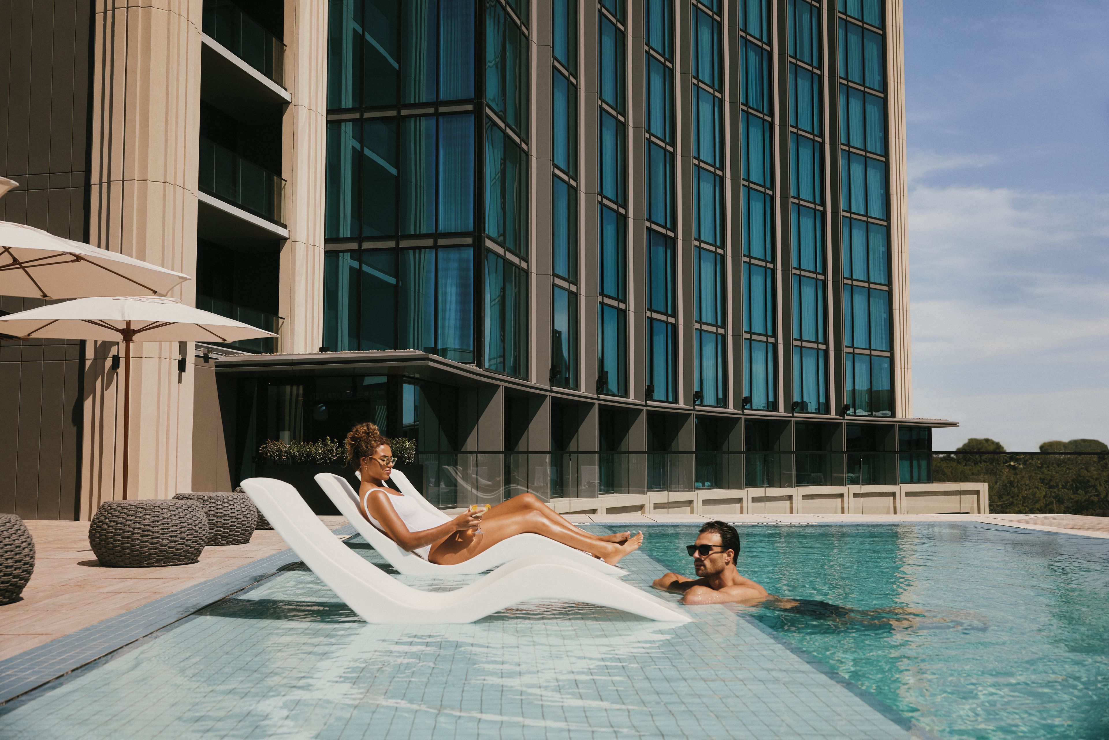 Un hotel moderno con piscina, sillones de descanso y sombrillas.