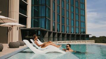 Un hotel moderno con piscina, sillones de descanso y sombrillas.
