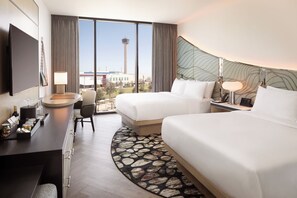 Een hotelkamer met twee bedden, een bureau met lamp, een stoel en uitzicht op een toren.