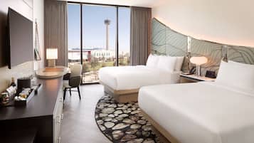 A hotel room with a bed, a desk, a chair, a TV, and a view of a tower.