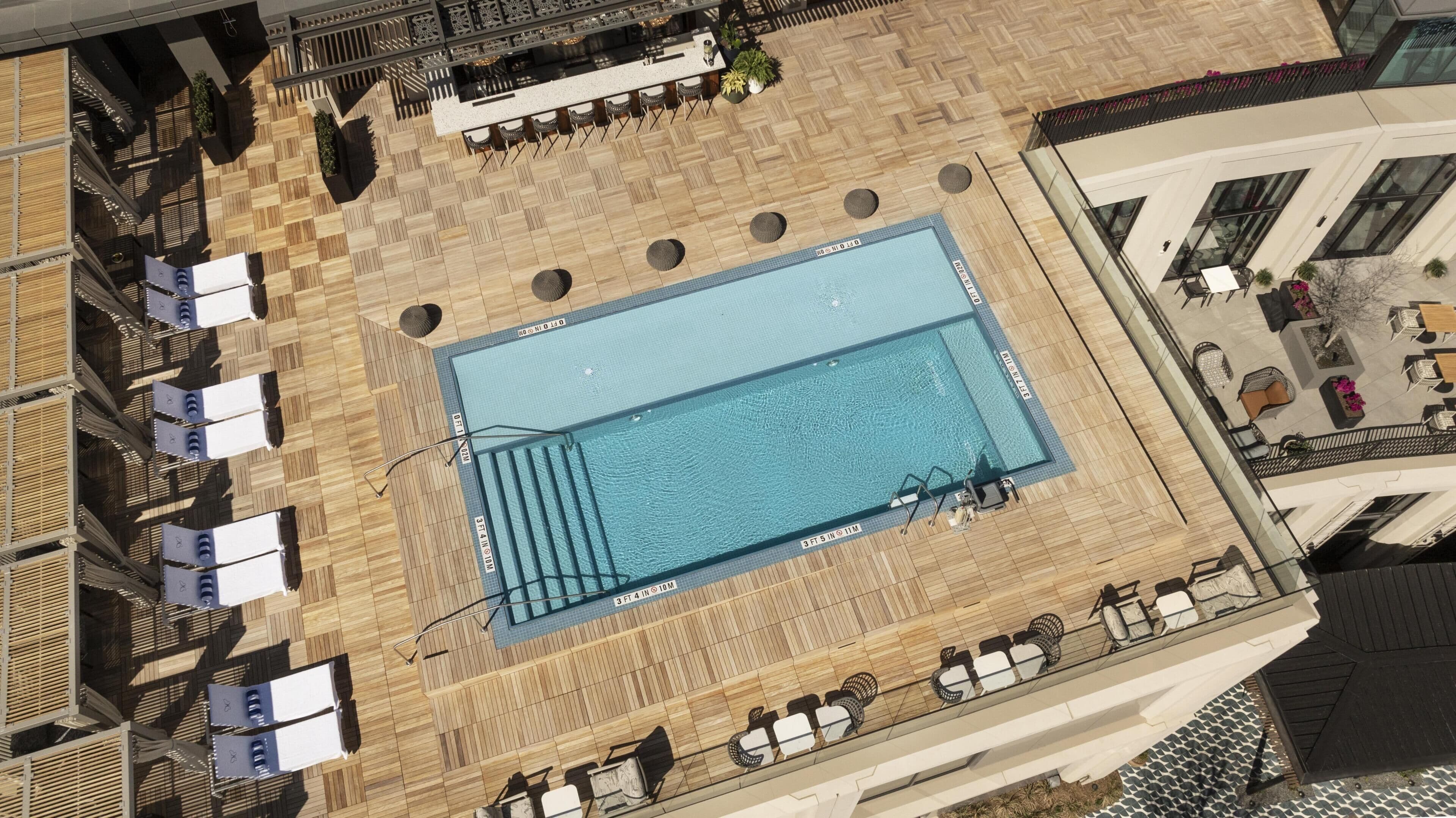 A rooftop pool with a wooden deck, lounge chairs, and a bar area.