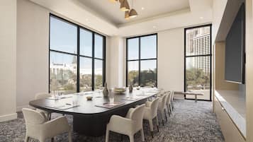 Un salón de conferencias con una gran mesa, múltiples sillas y amplios ventanales con vistas a la ciudad.