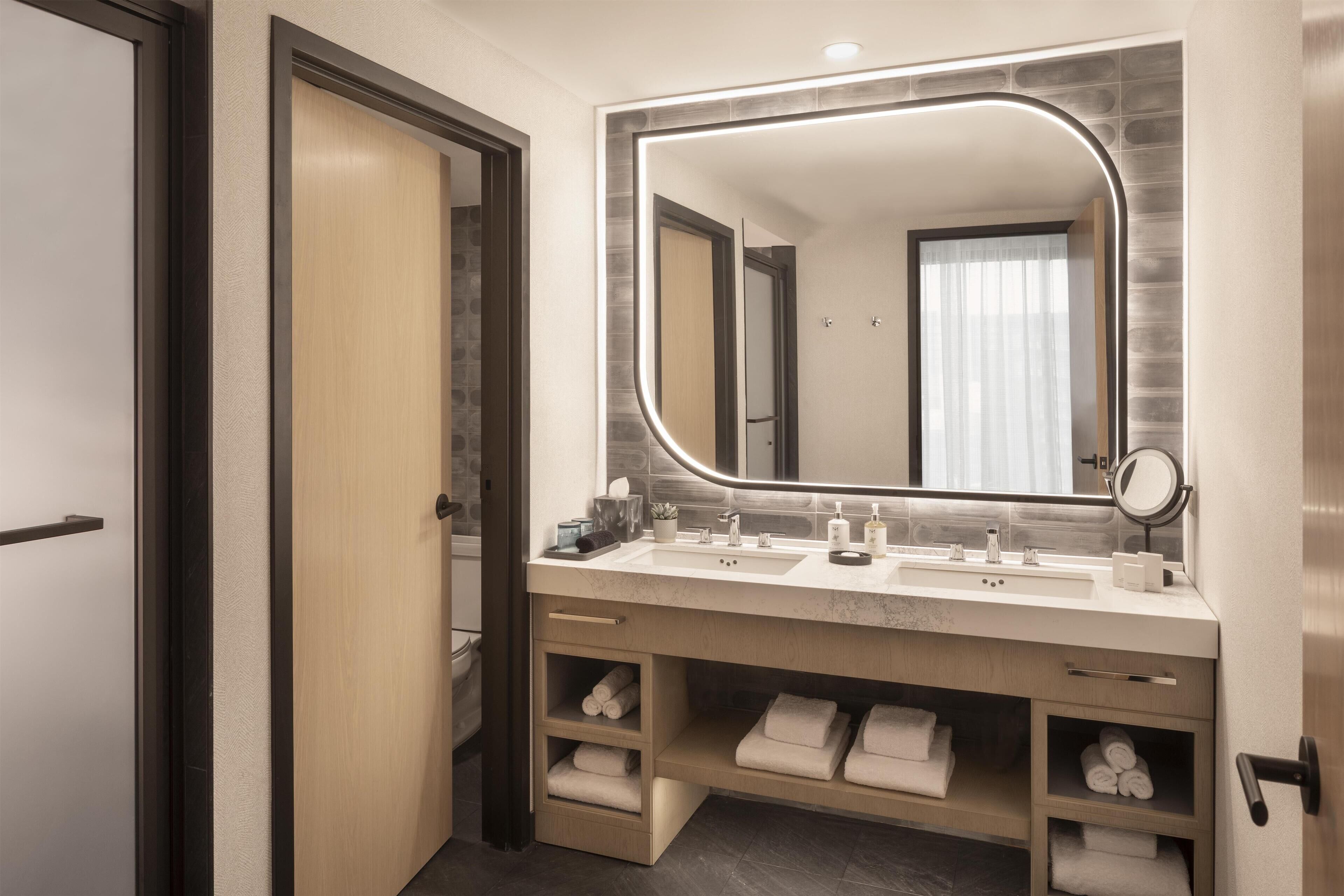 Une salle de bain moderne dotée d’un grand miroir, de deux lavabos et de porte-serviettes intégrés.