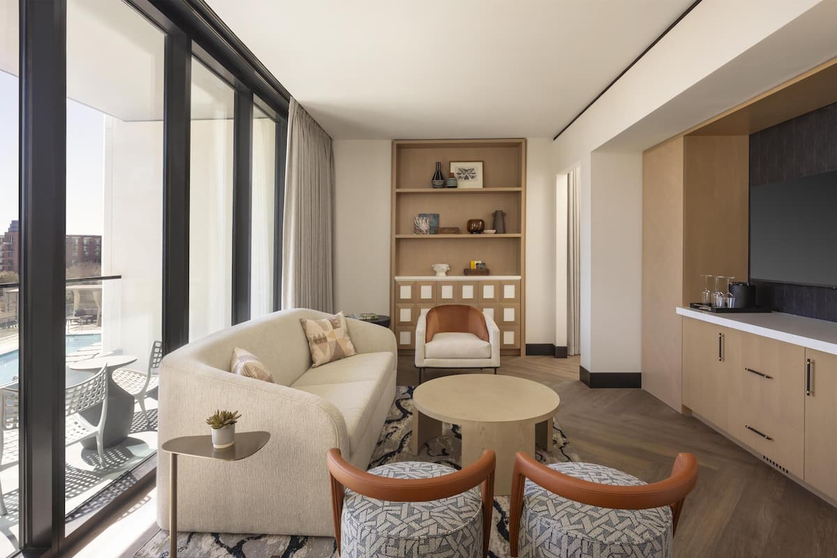 Una sala moderna con un sofá, dos sillones, una mesita de centro y una zona de comedor con una mesa y sillas. Cuenta con una cocina con armarios y una encimera.