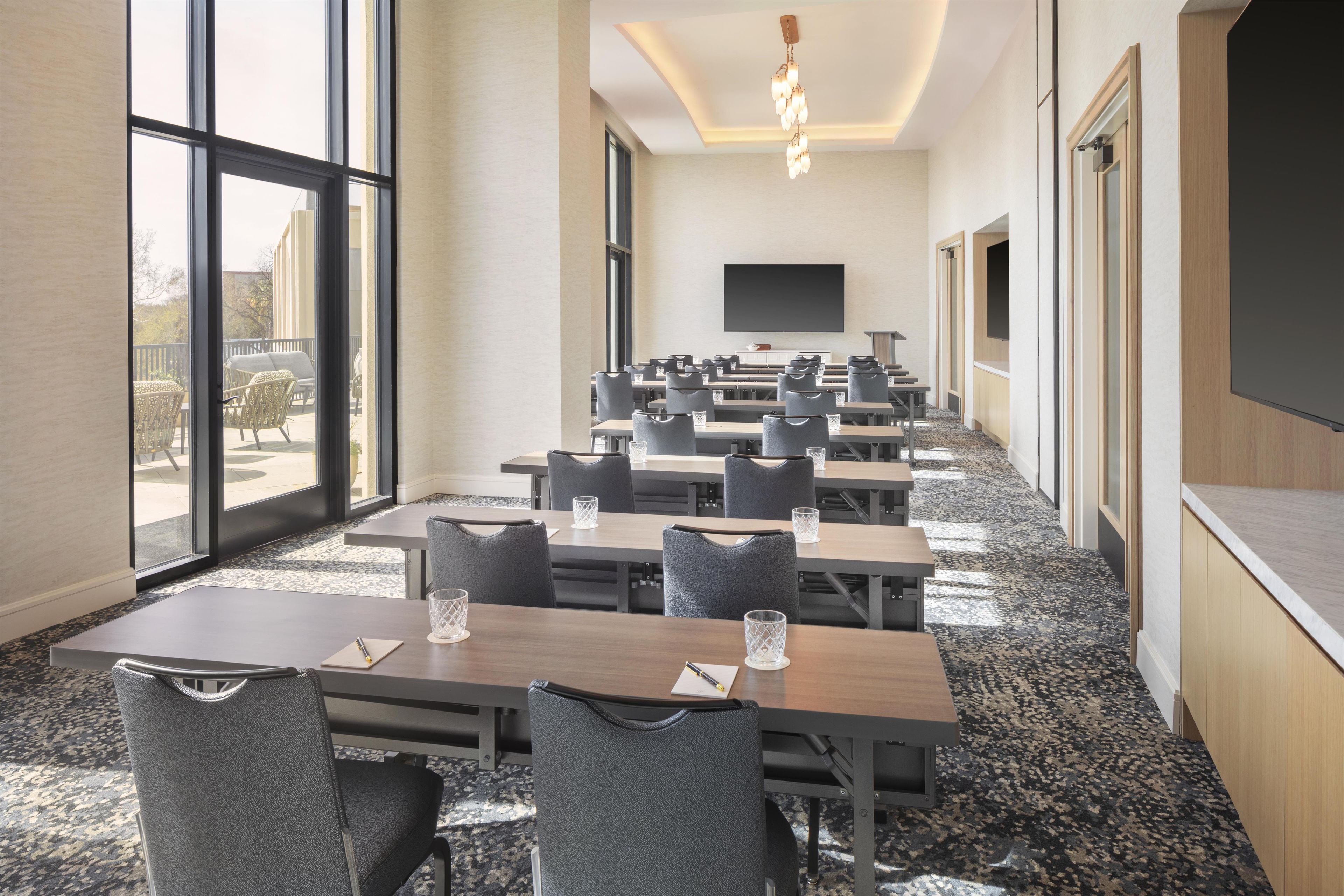 A conference room with tables and chairs, large windows, a flat-screen TV, and a carpeted floor.