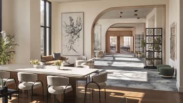 A spacious dining area with a long table and chairs, a large abstract painting on the wall, and a view of the dining area through an arched doorway.