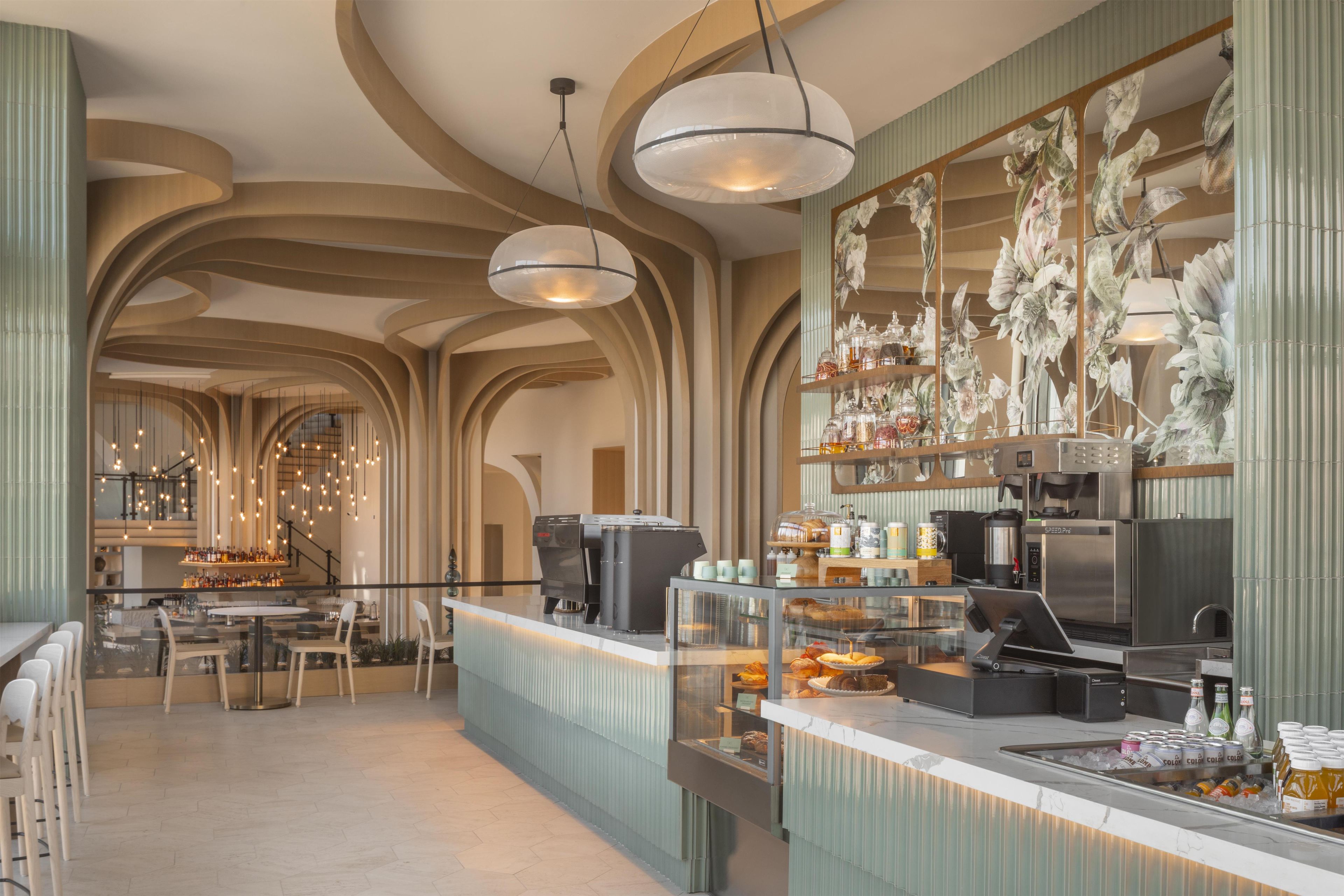 A modern bar area with a coffee machine, a display of pastries, and a variety of bottles.