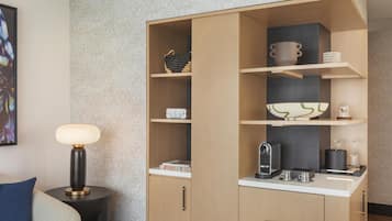 A compact living space with a built-in kitchenette, a small side table with a lamp, and a sofa with a cushion.