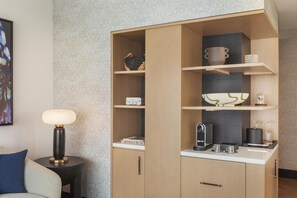 Een knus verblijf met een geïntegreerde kitchenette, een klein bijzettafeltje met lamp, en een bank met een kussen.