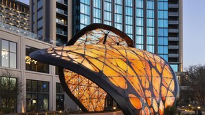 Un edificio moderno con una fachada de vidrio curva distintiva y una gran escultura iluminada al frente.