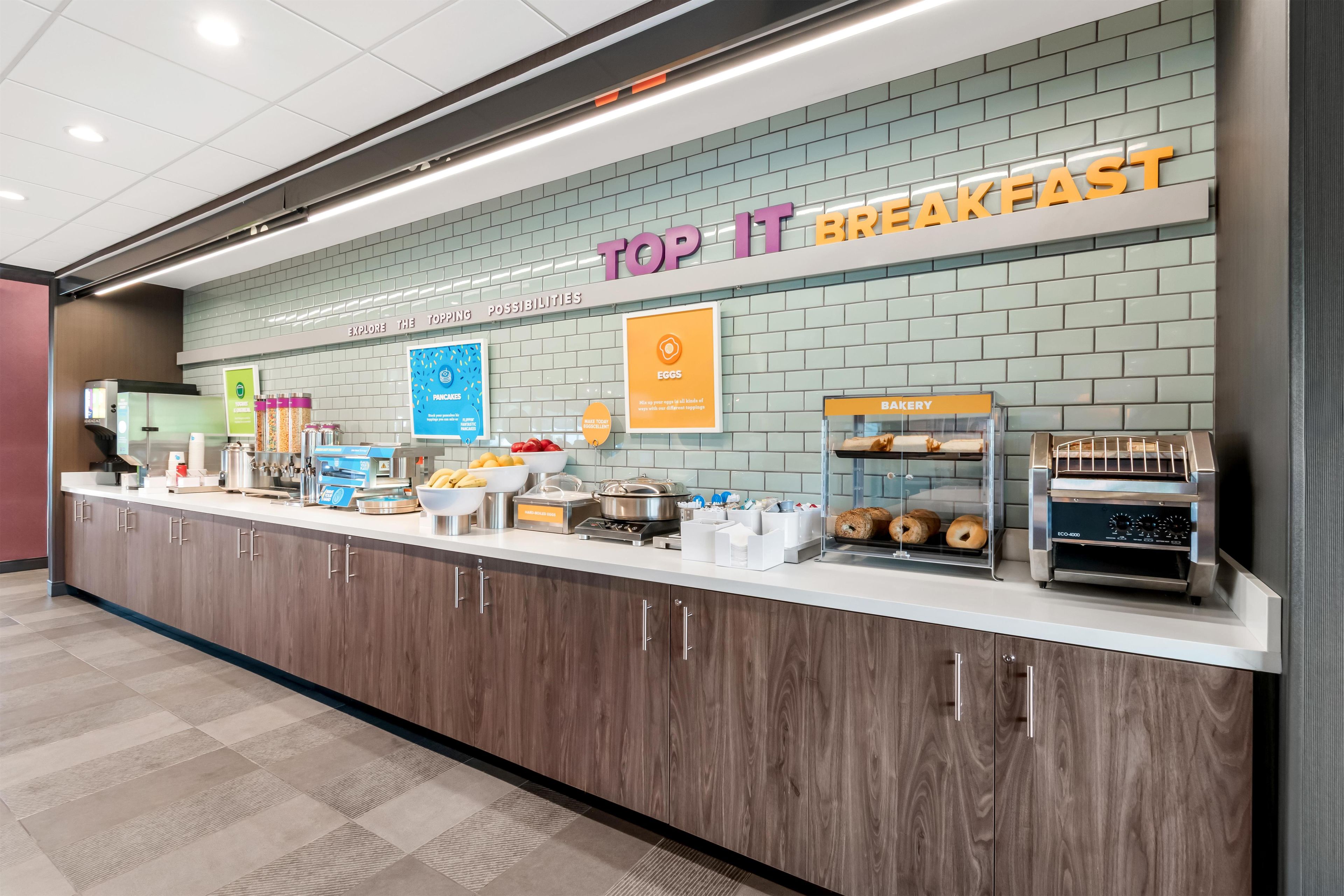 Estación de desayuno con un letrero que dice 'TOP IT BREAKFAST' y diversas opciones de comida.