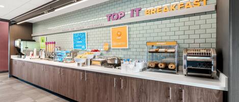 Estación de desayuno con un letrero que dice 'TOP IT BREAKFAST' y diversas opciones de comida.