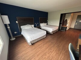 Una habitación de hotel con dos camas, un escritorio, una silla y una lámpara.