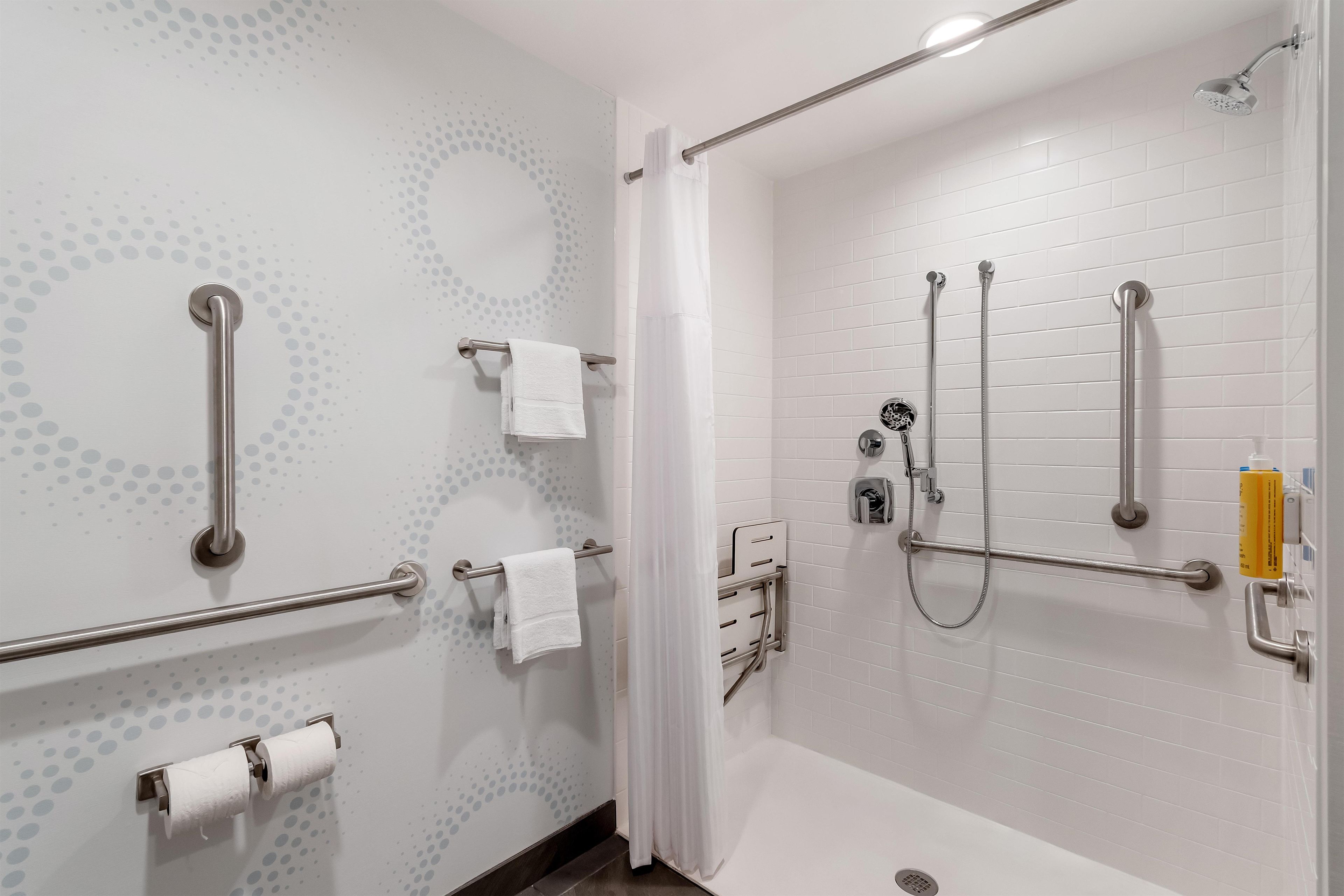 A bathroom with a walk-in shower, grab bars, a towel rack, and a toilet paper holder.