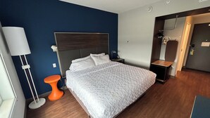 Habitació d'hotel amb llit, una tauleta de nit, una làmpada i una porta al bany.